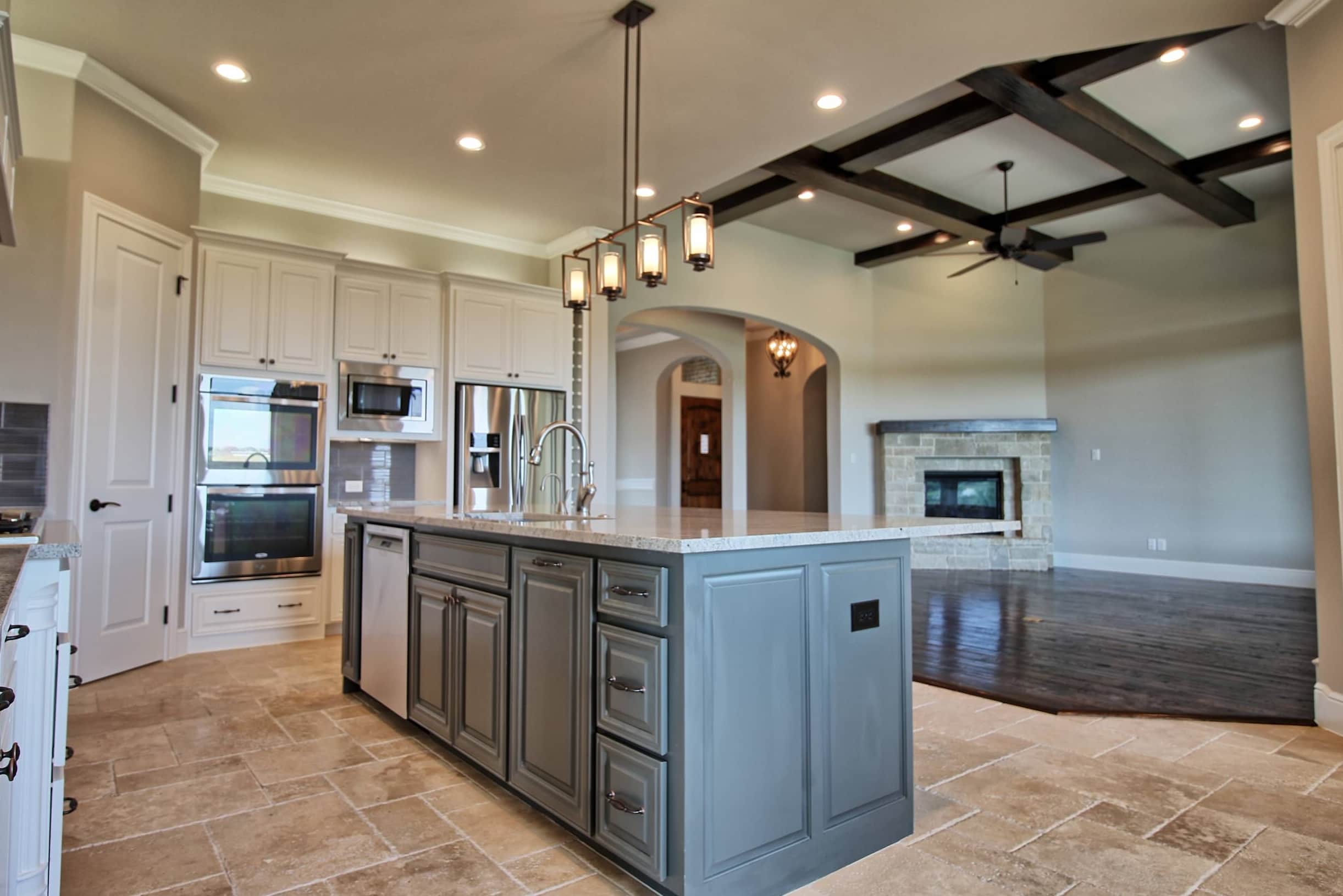Modern custom kitchen by Oakmark Signature Homes with contrasting cabinetry, oversized island, pendant lighting, and open living room with stone fireplace.