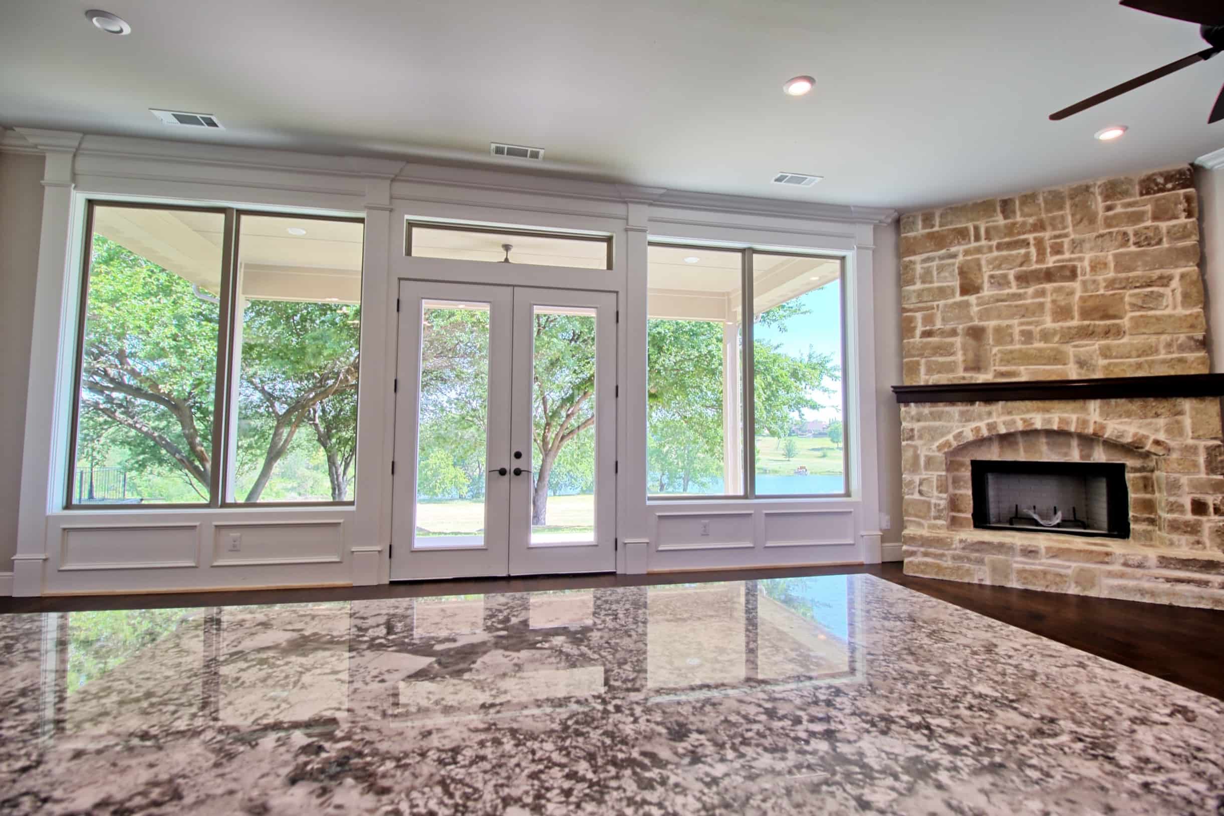 Luxury living room in an Oakmark Signature Homes custom build featuring floor-to-ceiling windows, stone fireplace, and elegant French doors overlooking scenic views.