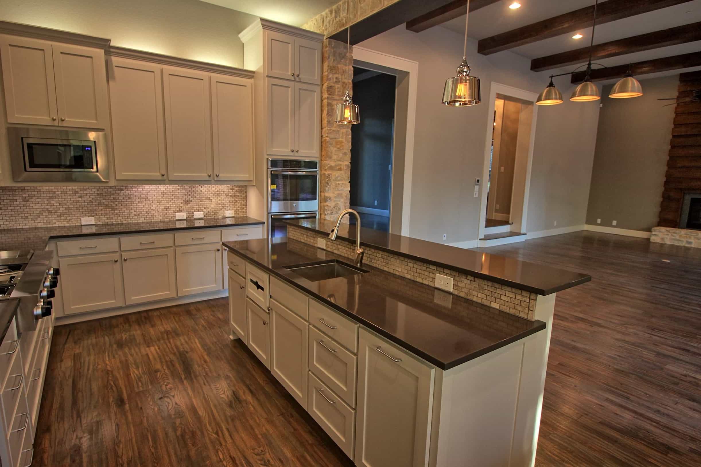Custom kitchen by Oakmark Signature Homes featuring quartz countertops, white cabinetry, stone accents, and open-concept design with hardwood floors.