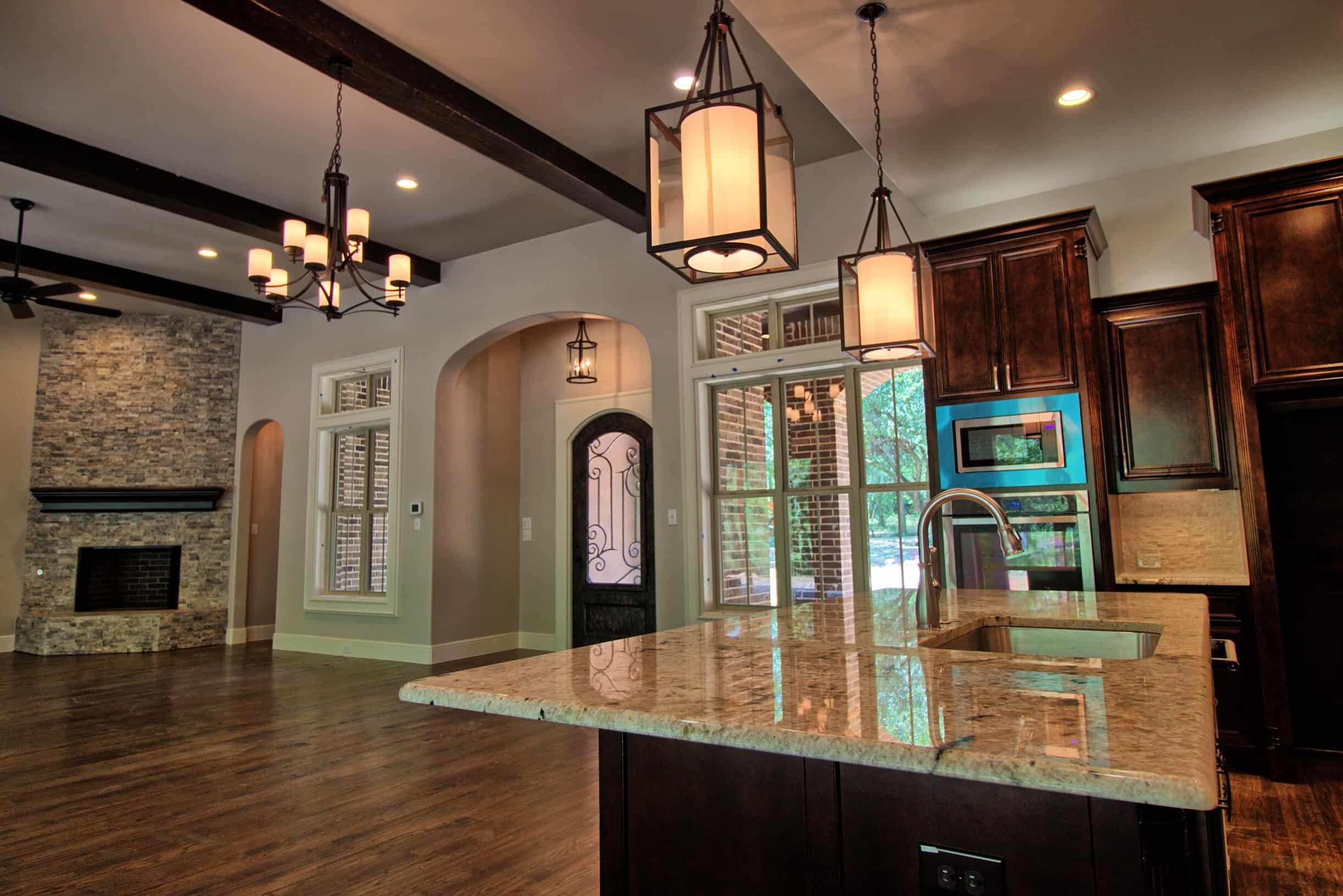 Luxury Oakmark Signature Homes living room and kitchen with stone fireplace, exposed beams, and granite island under designer pendant lights.
