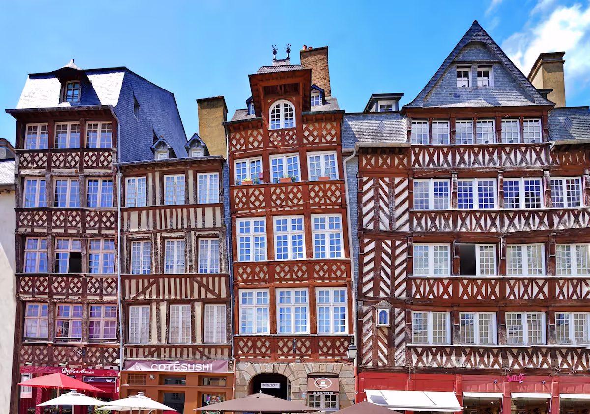 Façades de maisons à colombages avec fenêtres multiples sous un ciel bleu, typique de la ville de Rennes en Bretagne.