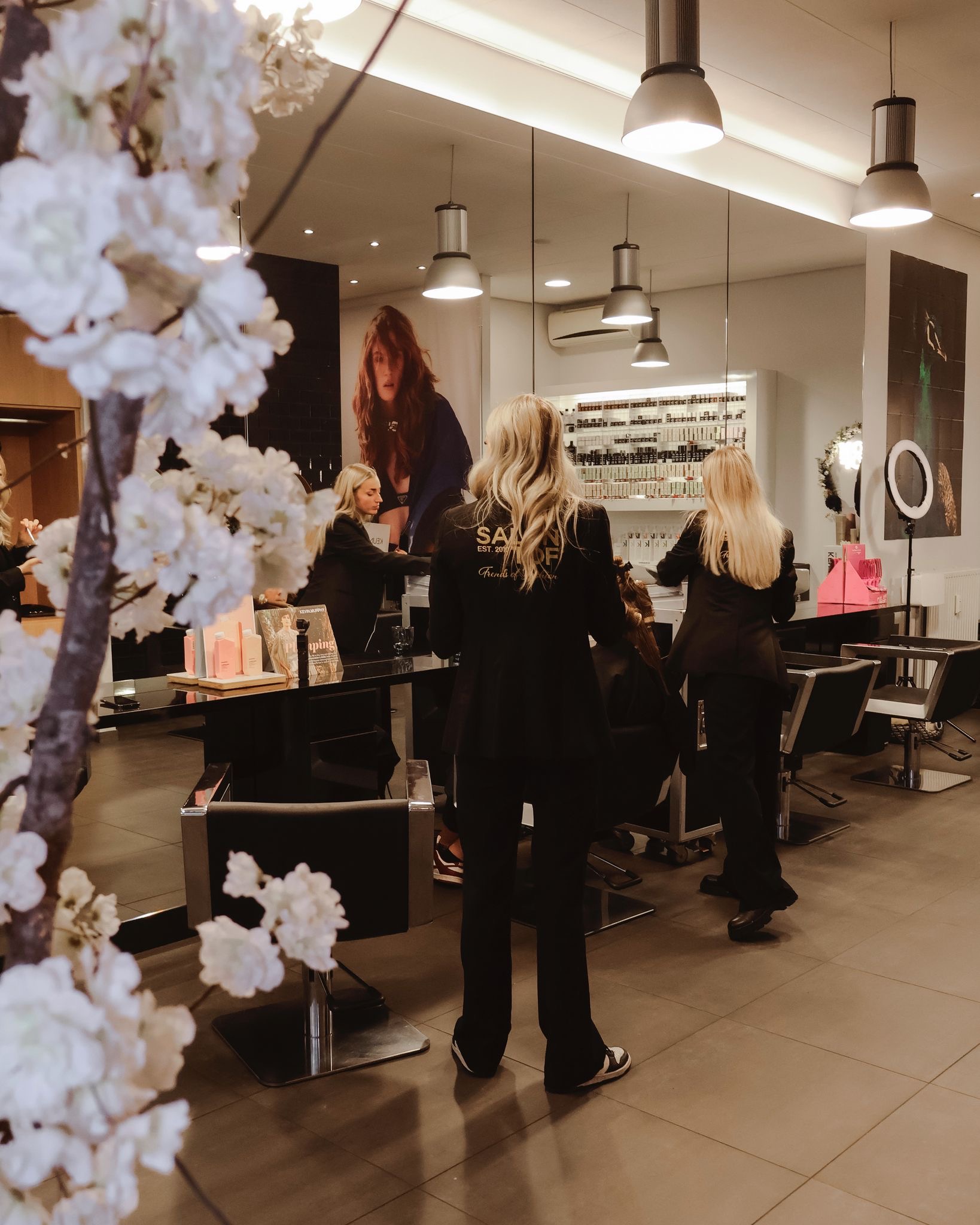 Interieur van een moderne kapperszaak in 's-Hertogenbosch met vrouwelijke kappers in zwarte kleding die klanten behandelen, omgeven door stijlvol meubilair en heldere verlichting.