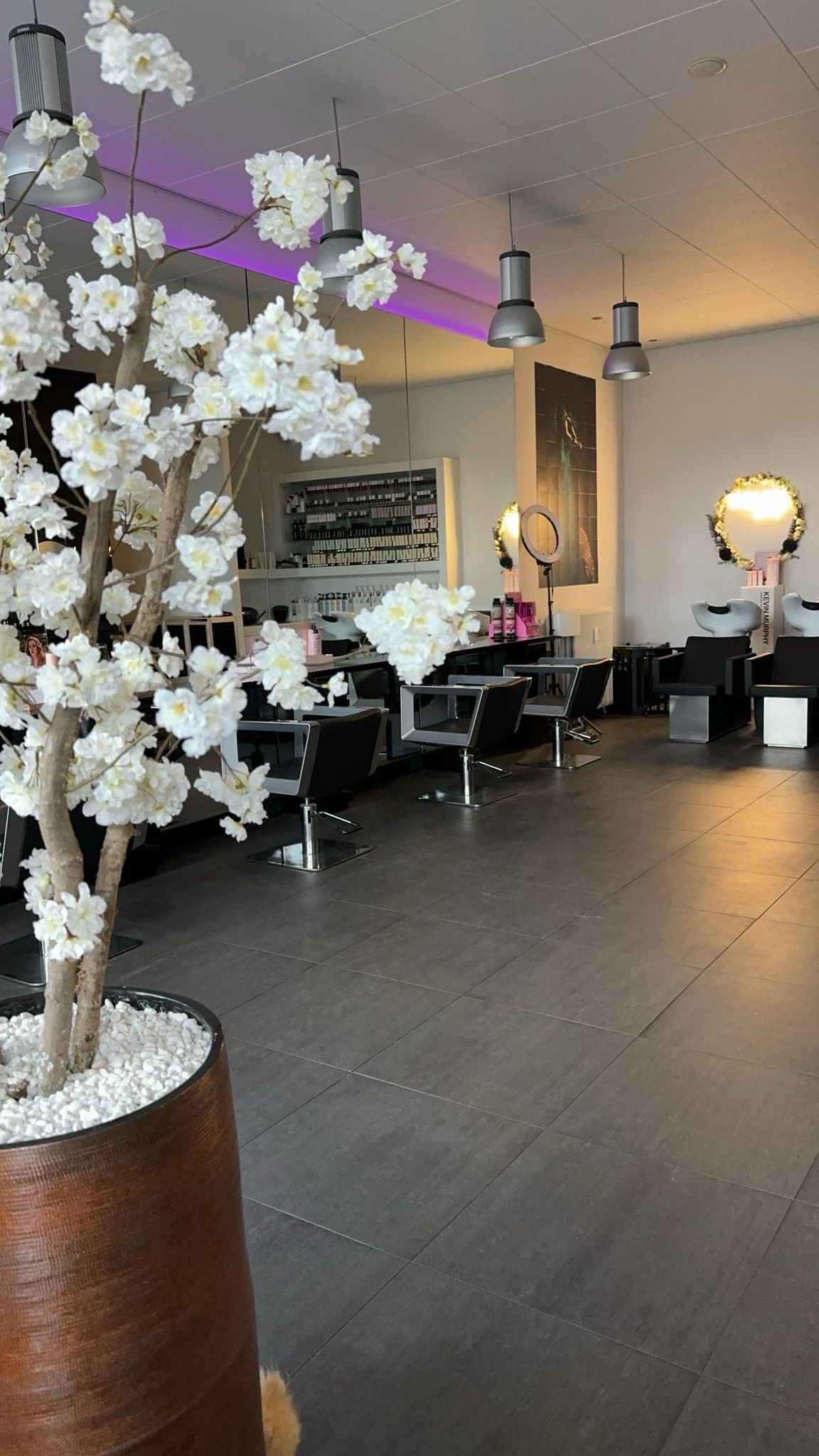 Interieur van een moderne kapperszaak in 's-Hertogenbosch met meerdere kapstoelen, hangende verlichting en een groot bloesemboom sierstuk op de voorgrond.