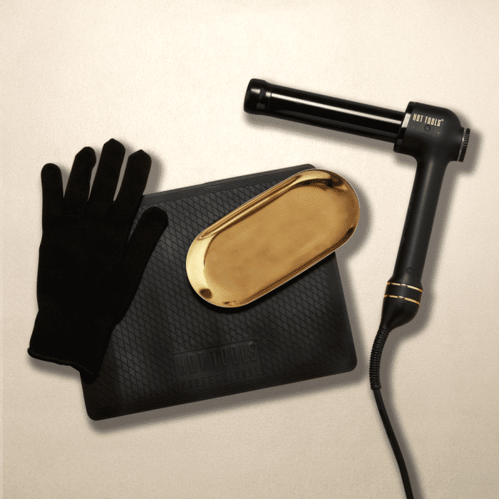 De afbeelding toont een professionele kappersuitrusting bestaande uit een zwarte hittebestendige handschoen, een stijltang naast een gouden hittebeschermende hoes en een zwarte antislip hittemat, typisch gebruikt door kappers in 's-Hertogenbosch.