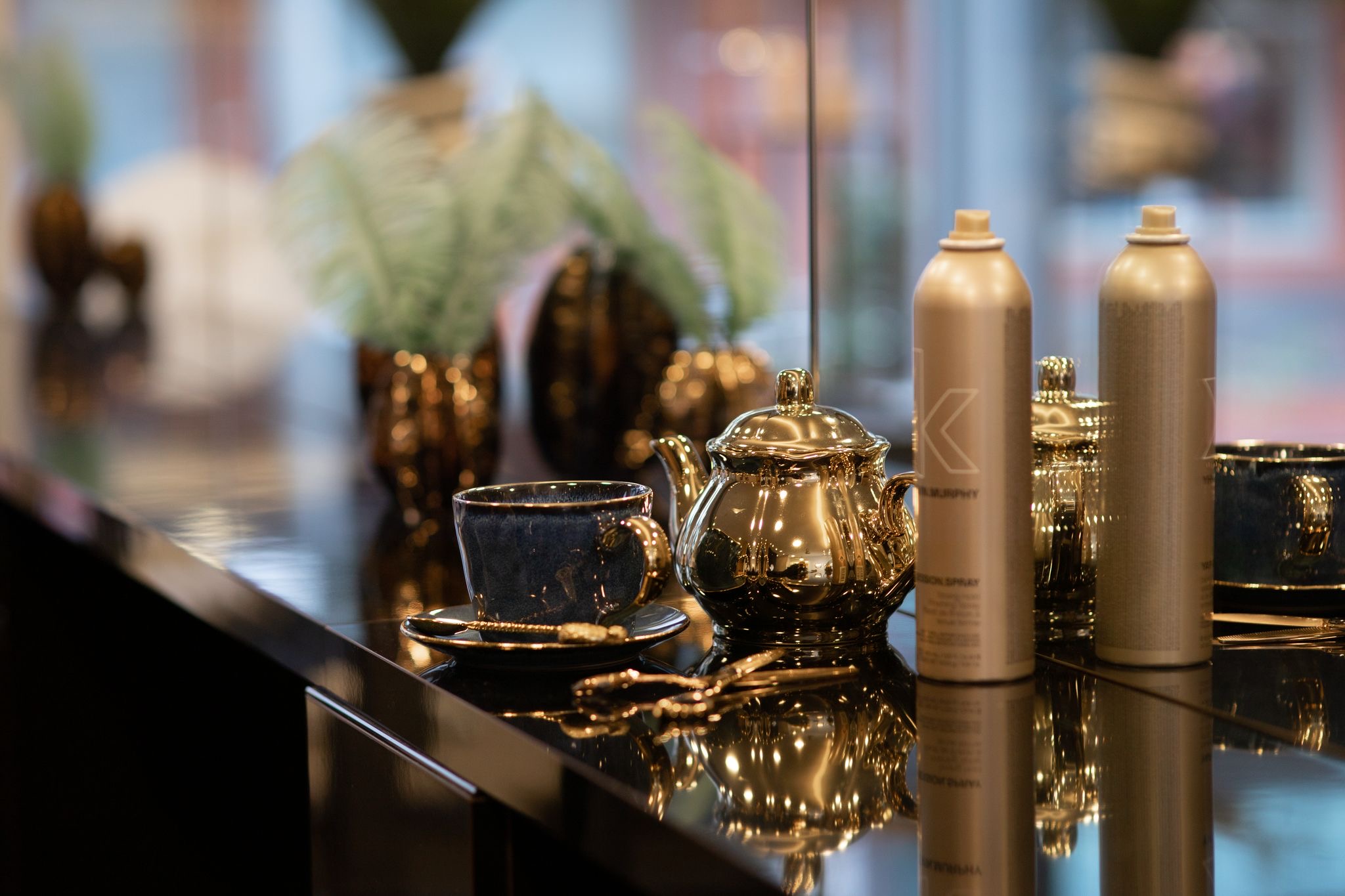 Een stijlvolle kapperszaak in 's-Hertogenbosch, uitgerust met glimmende theeservies en hoogwaardige haarsprayflessen, weerspiegelt elegantie op een glanzende zwarte balie.