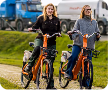 A couple of women standing next to each other on bikes.
