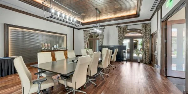 Modern conference room with a long black table, cream swivel chairs, wood flooring, and large windows with curtains.