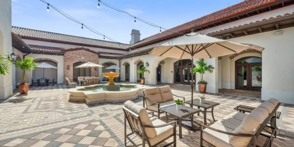 Sunlit courtyard with tiled flooring, outdoor seating area under umbrella, and a central water fountain.