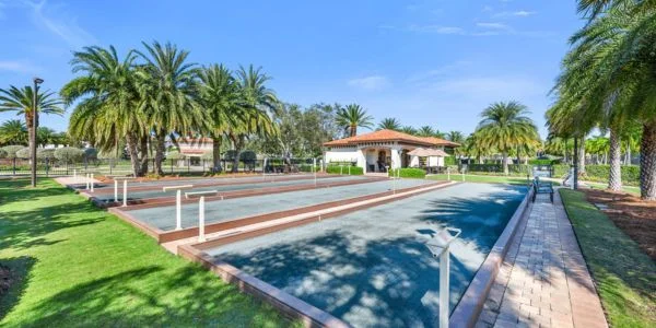 Outdoor bocce ball courts surrounded by palm trees under a clear blue sky with a small building in the background.