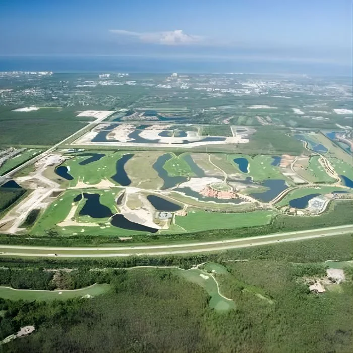 Aerial view of a golf course with several ponds, sand traps, and green fairways surrounded by natural vegetation under a partly cloudy sky.