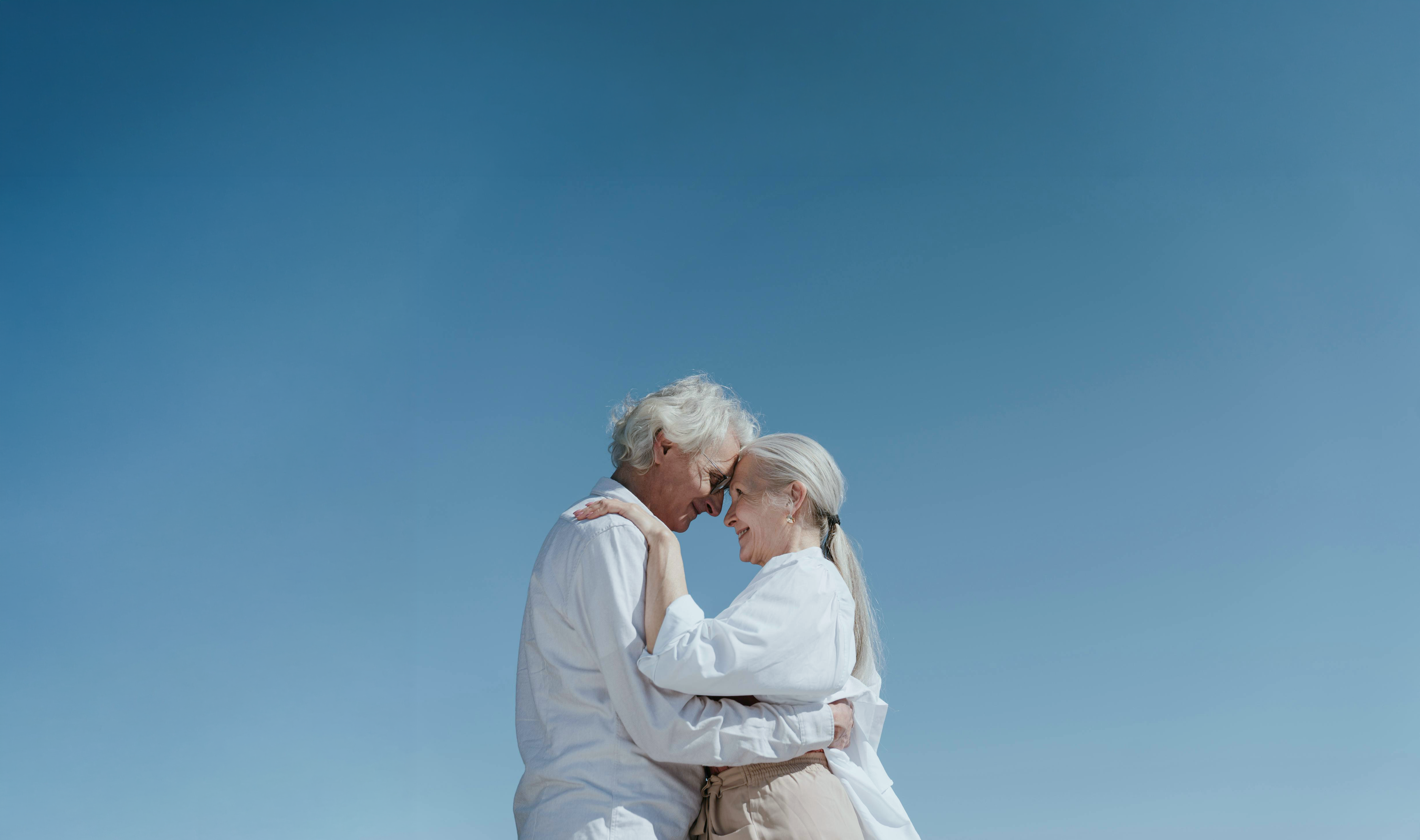 An older couple embracing outdoors beneath a blue sky.