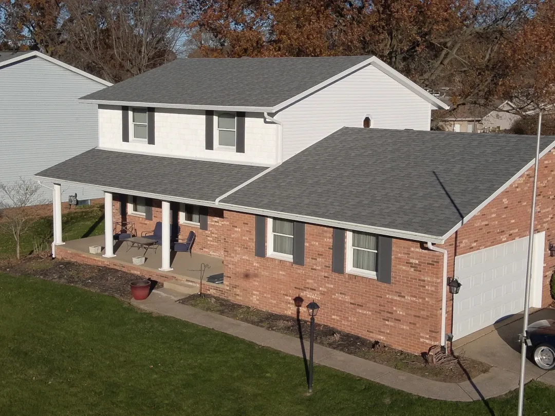 brick home with gray shingle roof and white gutters