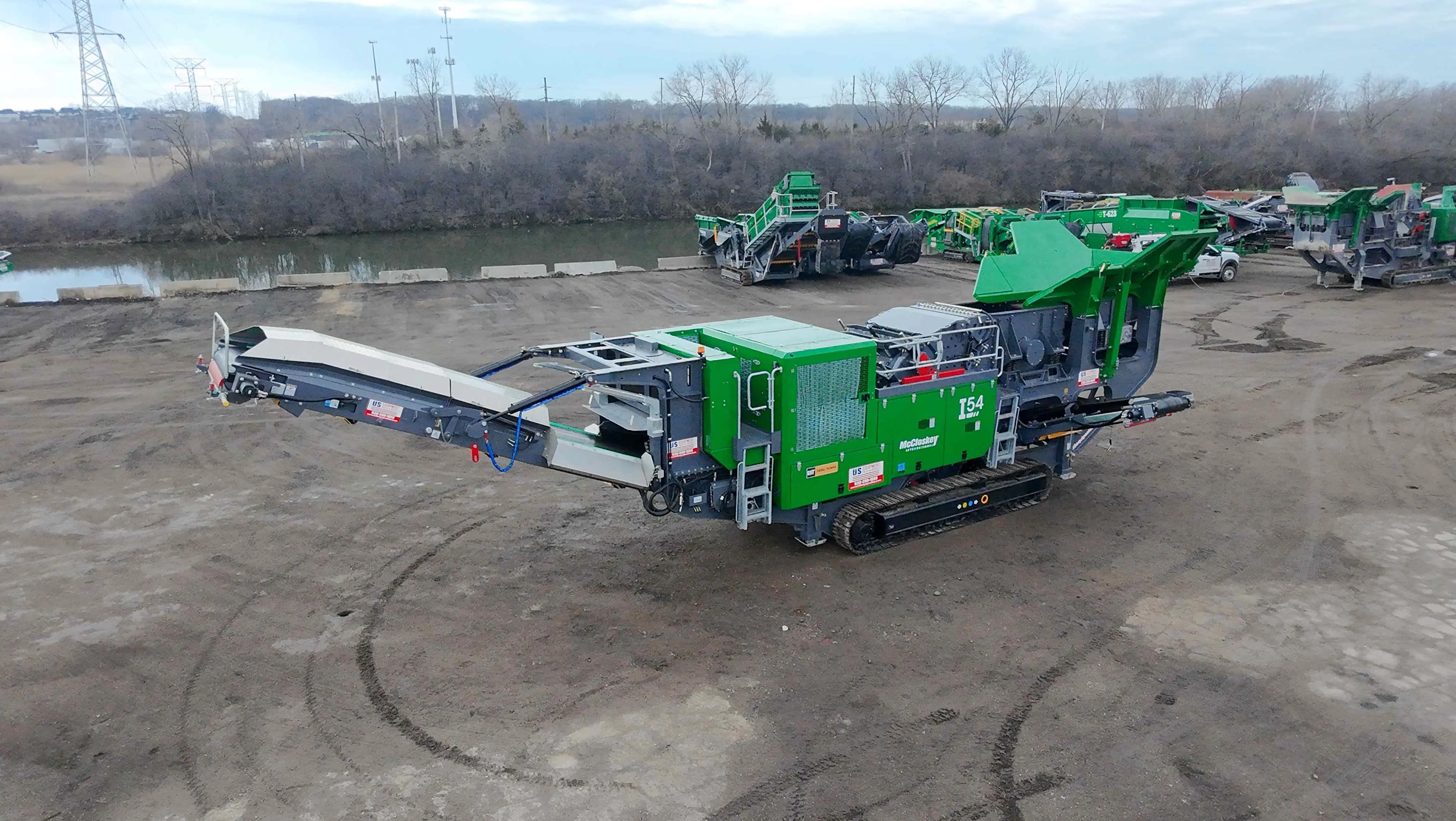 A powerful green track-mounted McCloskey I54 impact crusher, fully deployed on a job site with other green equipment visible in the background.