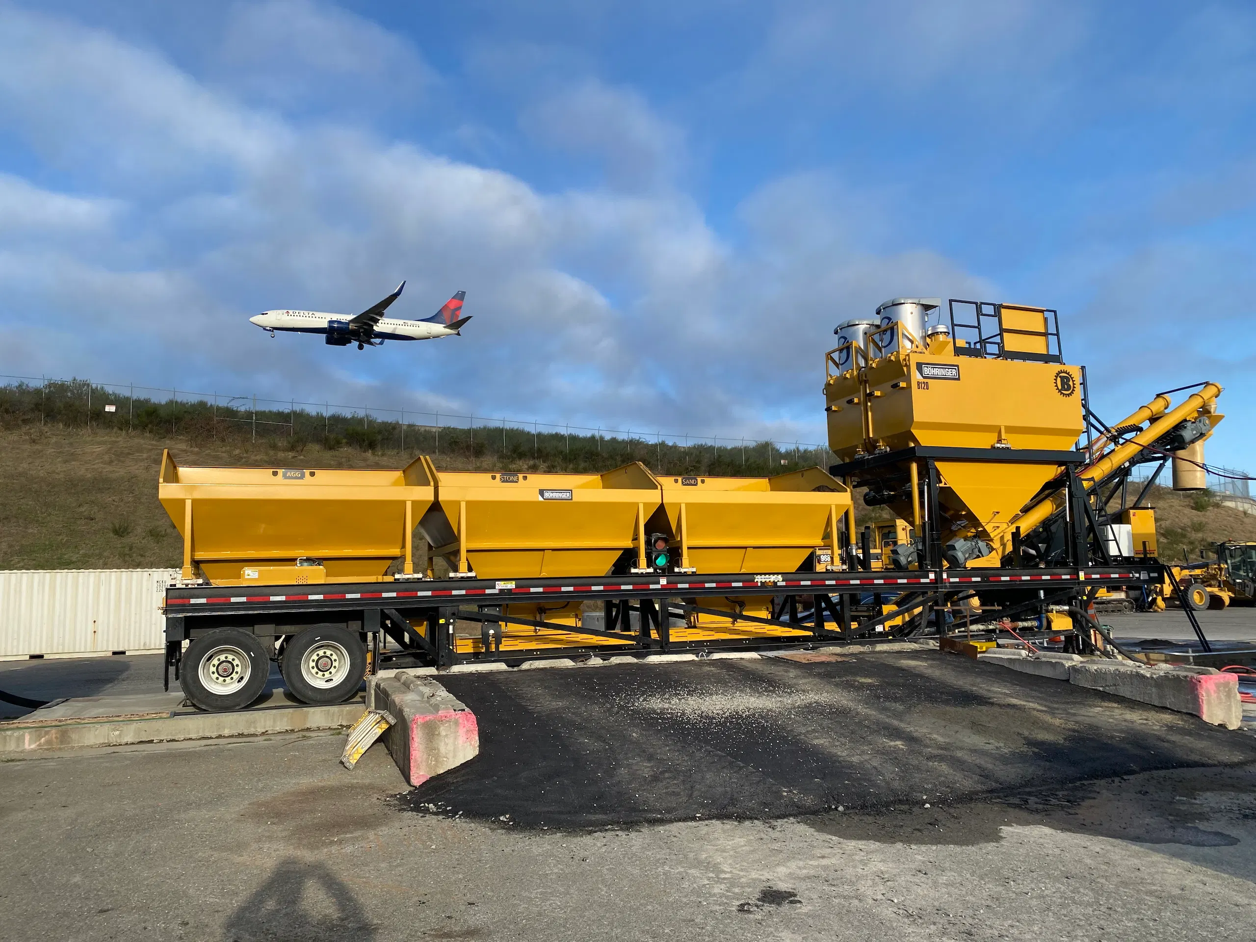 Bohringer portable processing plant set up near an airport runway as a commercial airplane passes overhead, showing mobile aggregate equipment in operation.
