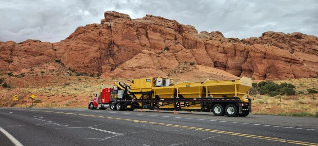 Semi-truck hauling a Bohringer portable processing plant along a desert highway with large red rock formations in the background, highlighting long-distance equipment transport.