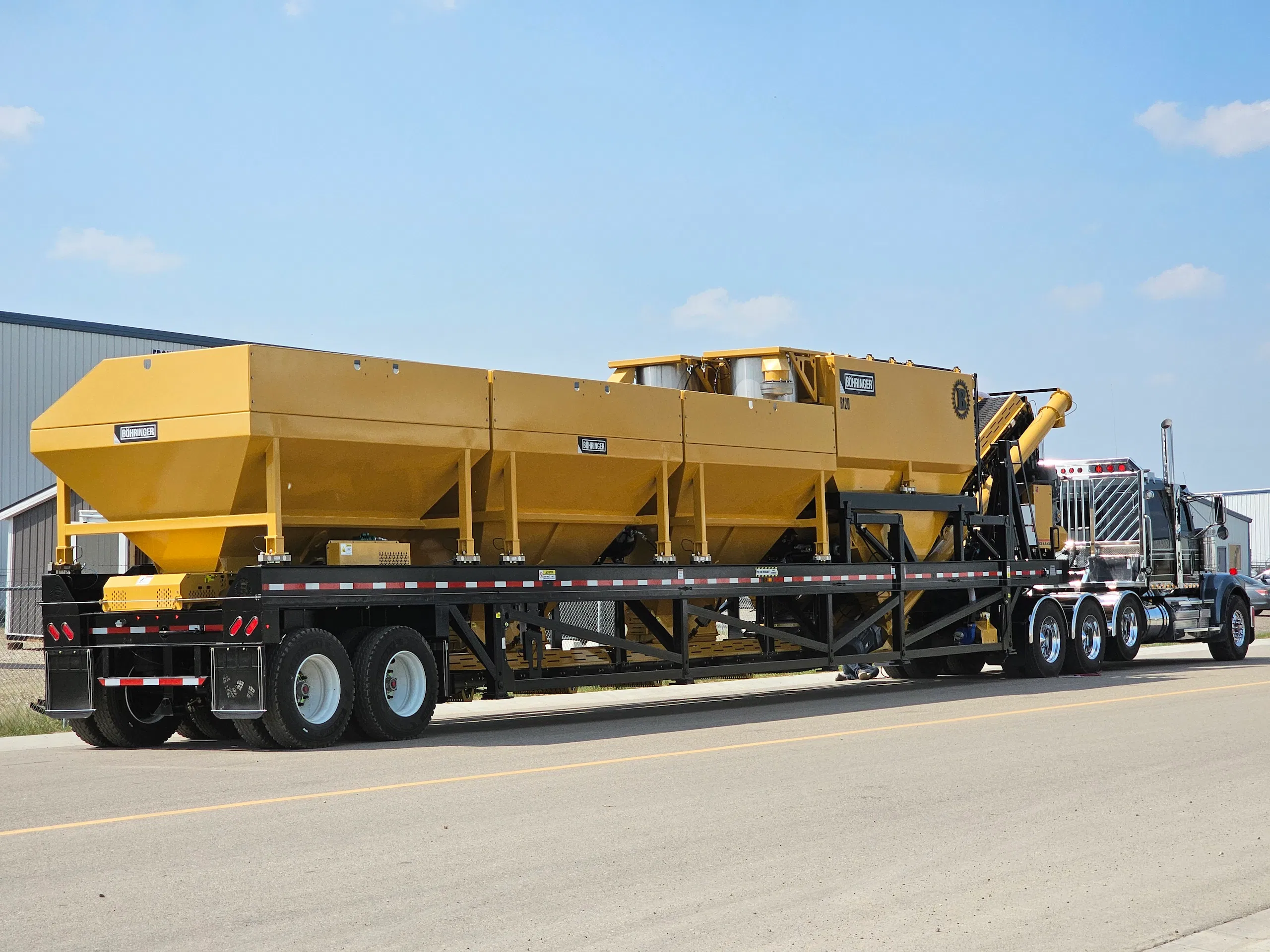 Bohringer portable processing plant loaded on a flatbed trailer for delivery, featuring multiple yellow hoppers and conveyors for aggregate production.