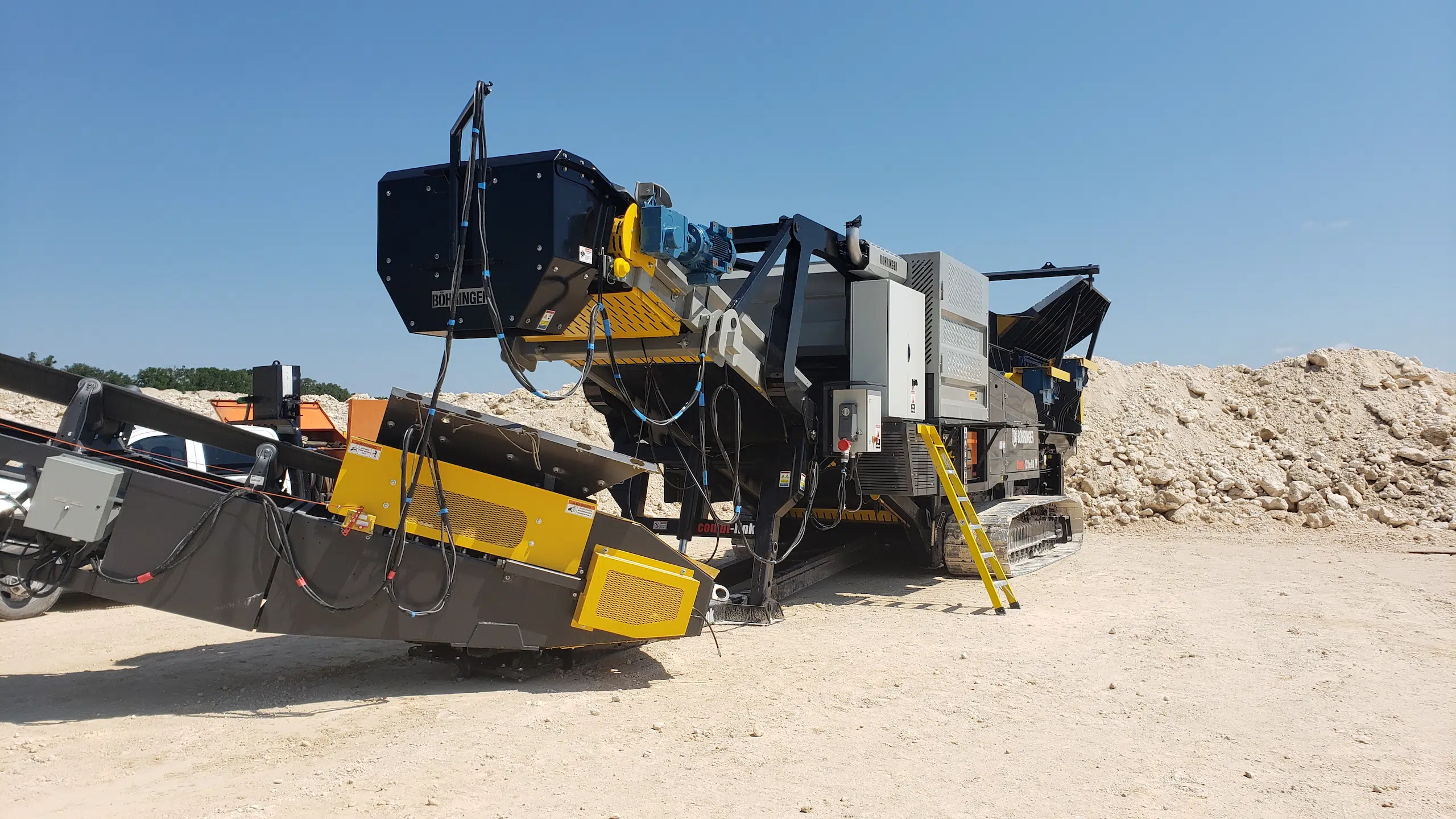 Close-up view of a Böhringer mobile impact crusher system with conveyors and tracked undercarriage, positioned on a limestone jobsite.