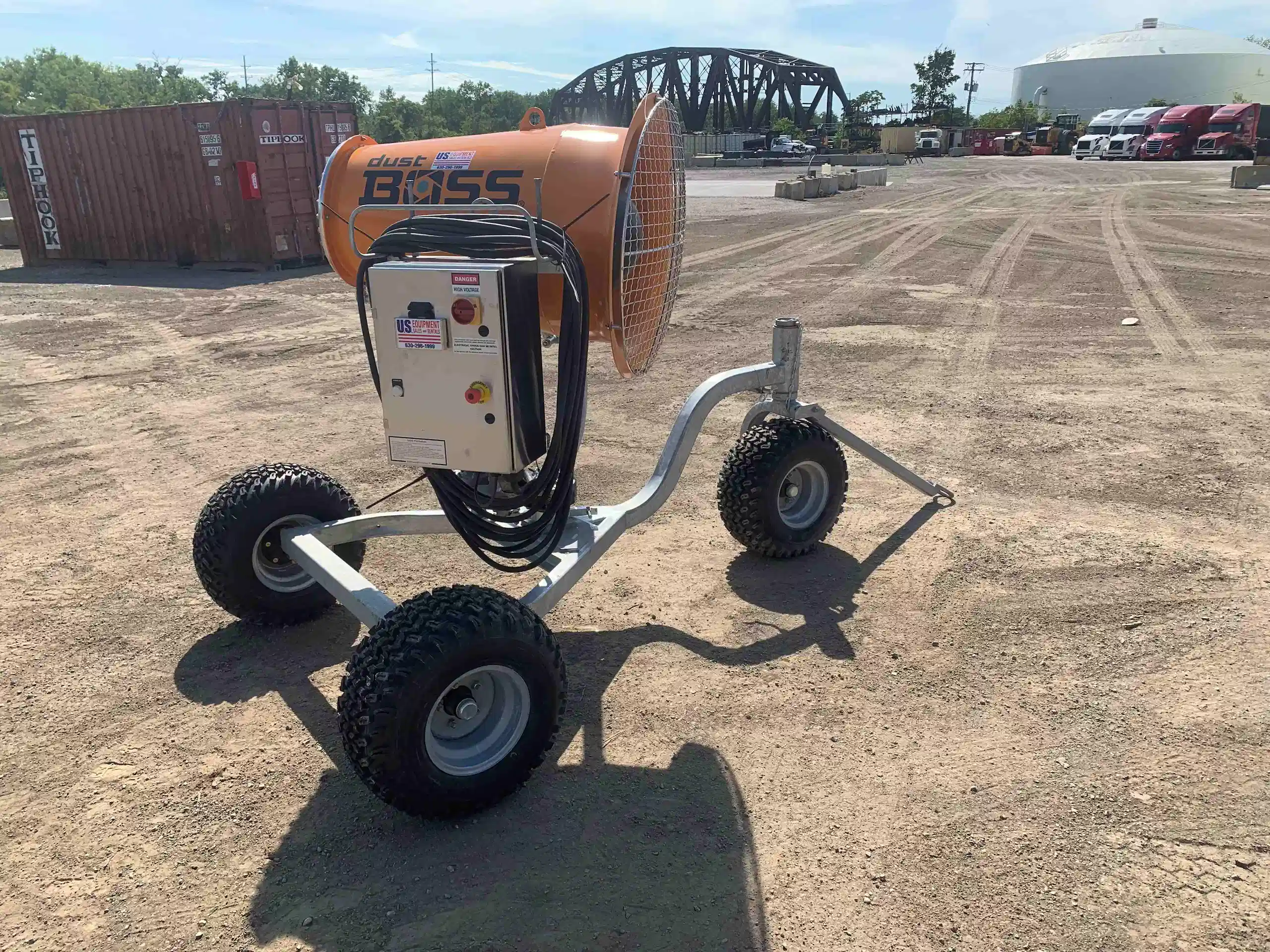 Dust suppression cannon positioned near a river and industrial site, equipped with hose reel and control box for mobile dust control.