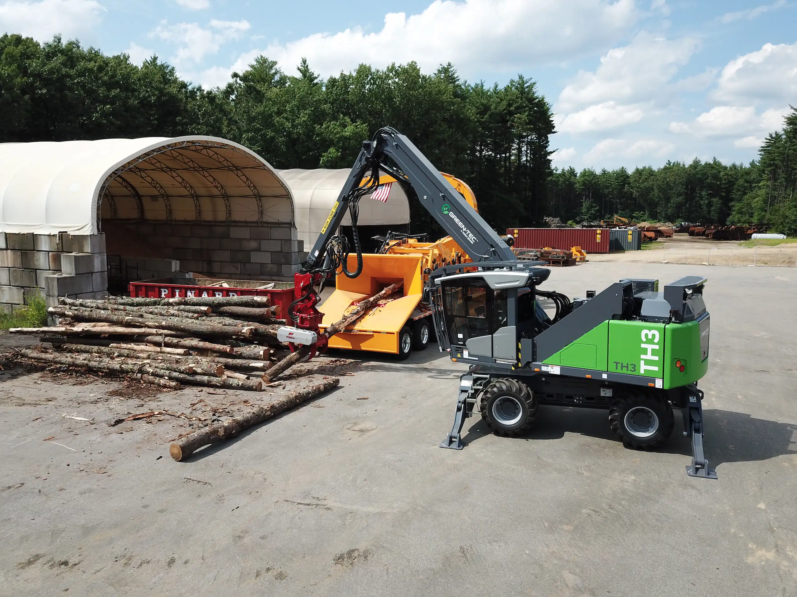 Green-Tec TH3 material handler feeding logs into CBI processing equipment, supporting efficient biomass and wood waste processing.
