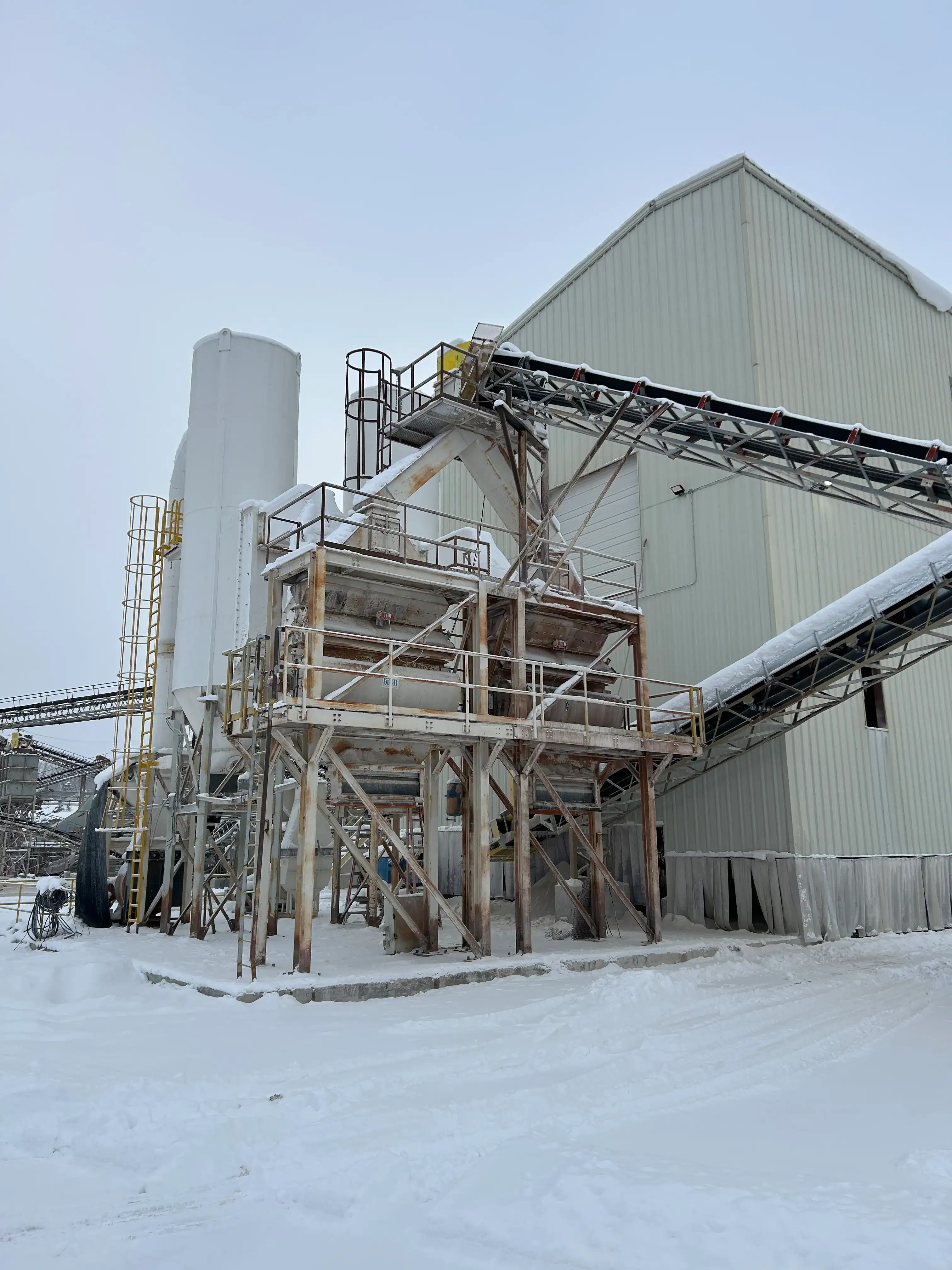 Fixed aggregate processing plant with conveyors and silos operating in winter conditions at an industrial site.