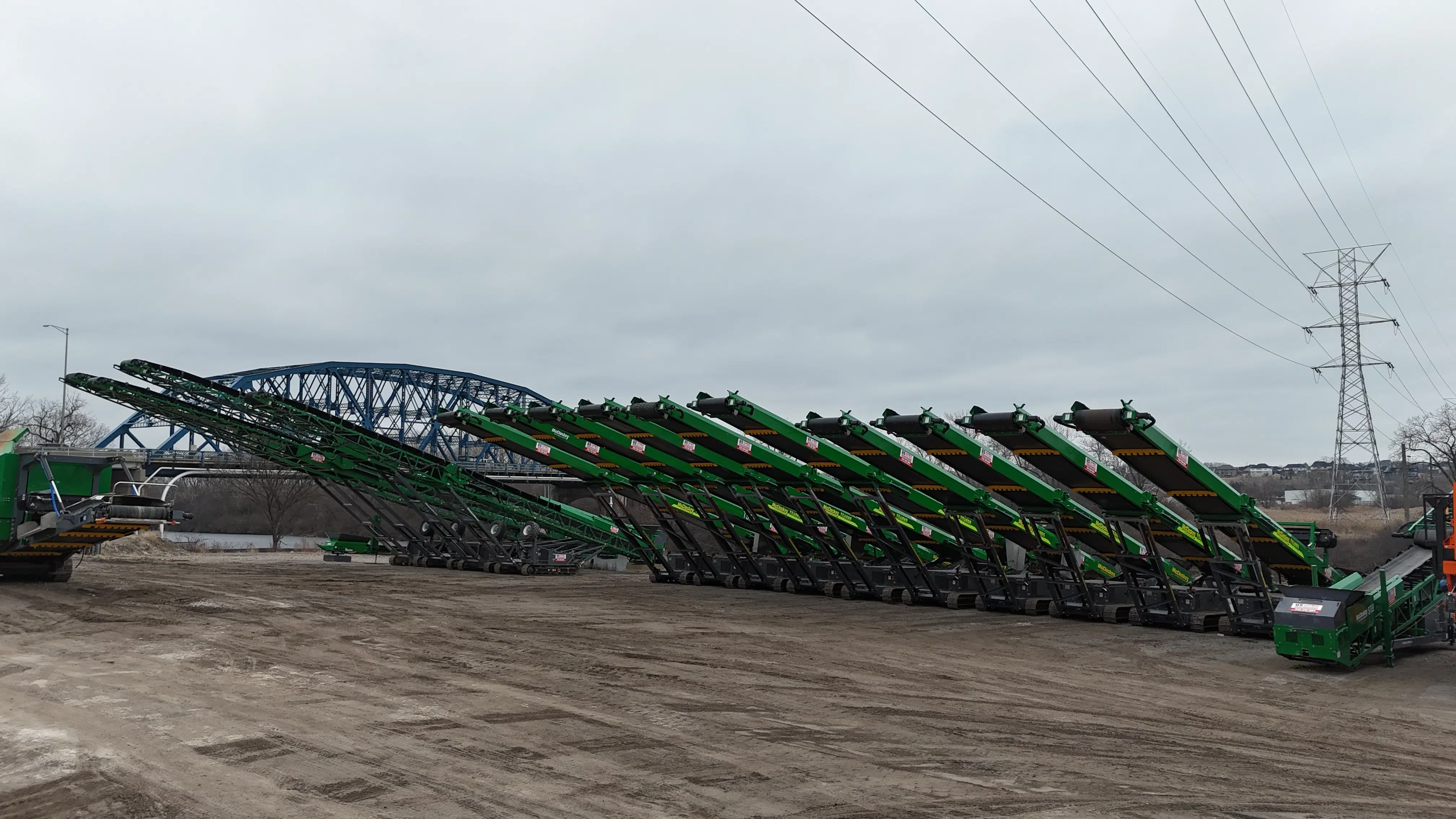 Large lineup of green stacker conveyors arranged in rows at US Equipment Sales yard, ready for deployment to quarry and construction sites.
