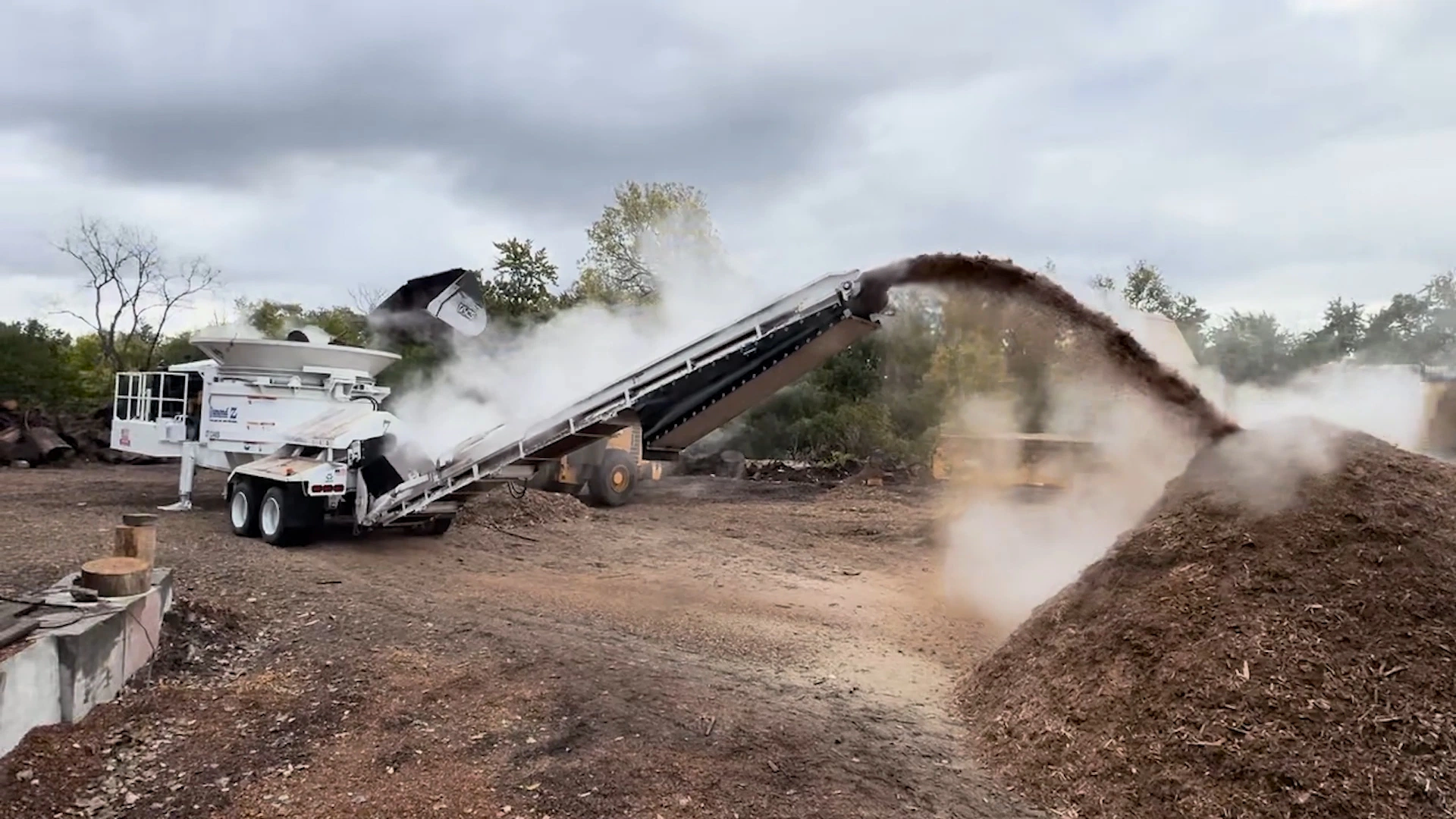 Diamond Z horizontal grinder processing wood debris and discharging mulch through its conveyor, creating a large steaming mulch pile on a forestry jobsite.Diamond Z horizontal grinder processing wood debris and discharging mulch through its conveyor, creating a large steaming mulch pile on a forestry jobsite.