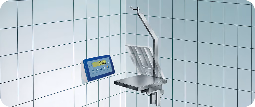 Wall-mounted digital scale display and adjustable stainless steel platform in tiled room corner.