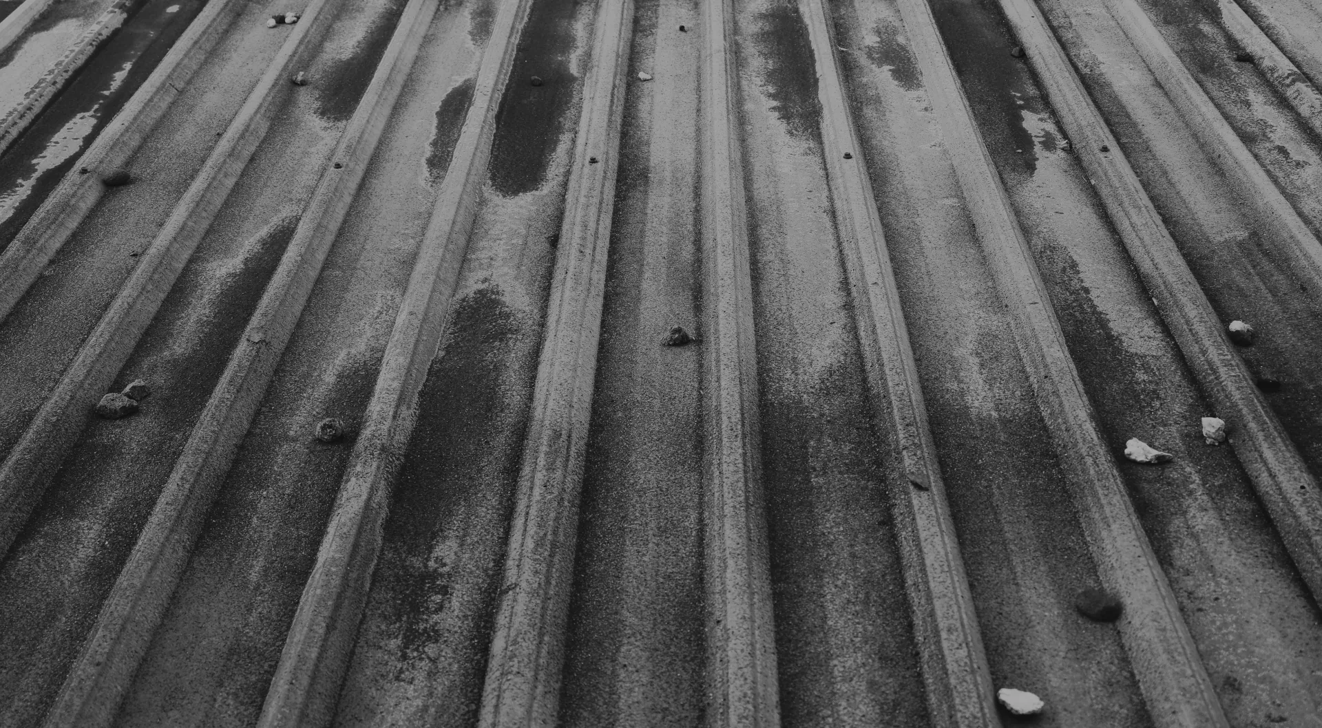Close-up of weathered metal roof panels with scattered small stones on the surface.