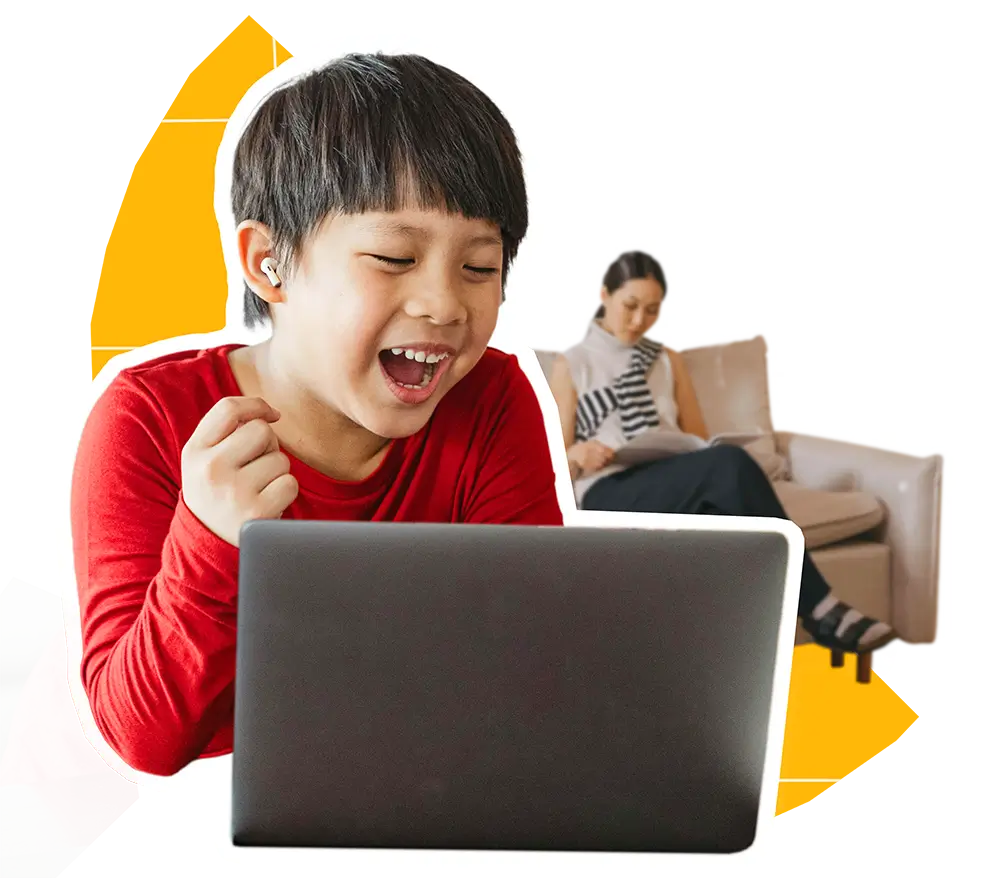 A young male student smiling and cheering at laptop while mother sits comfortably in the background
