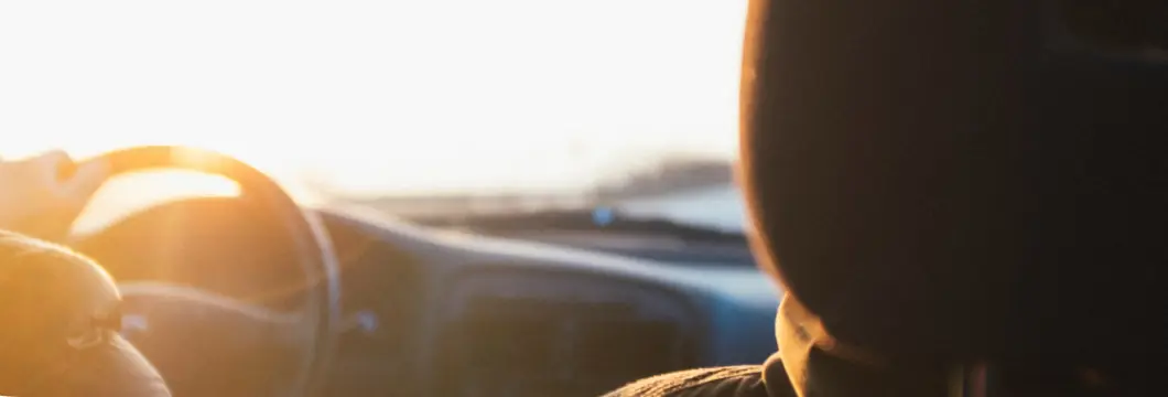 Mão de motorista no volante de um veículo ao pôr do sol