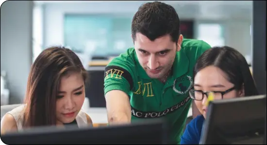 Teacher helping two students working at computers