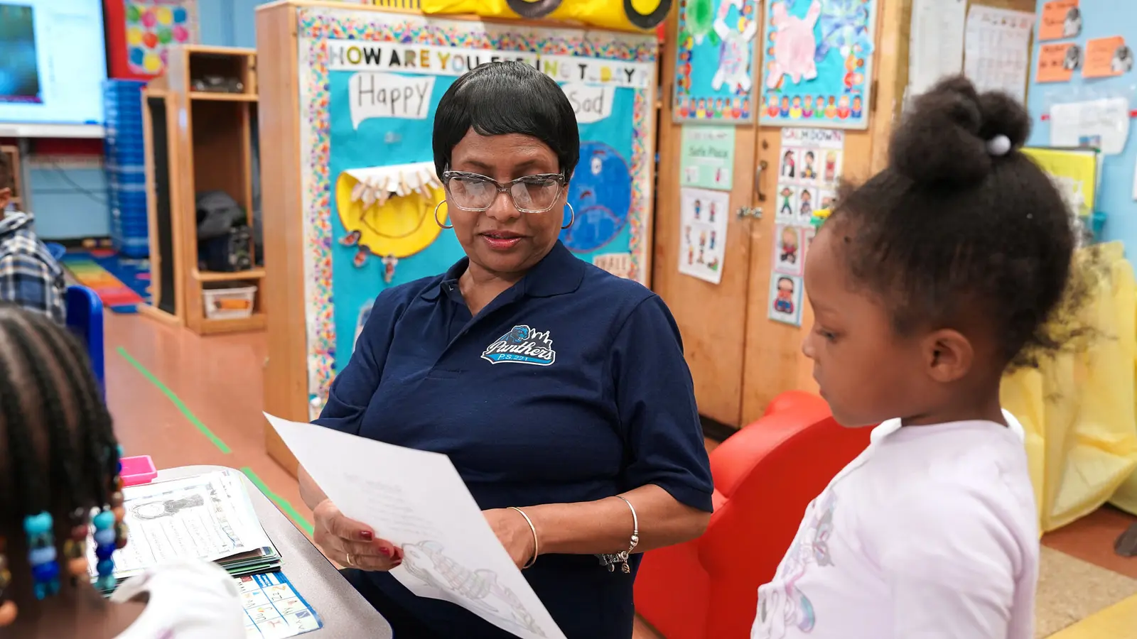 Teacher reviewing student work with young learner in classroom