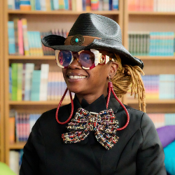 Tamu Francis smiling in library wearing hat and bow tie