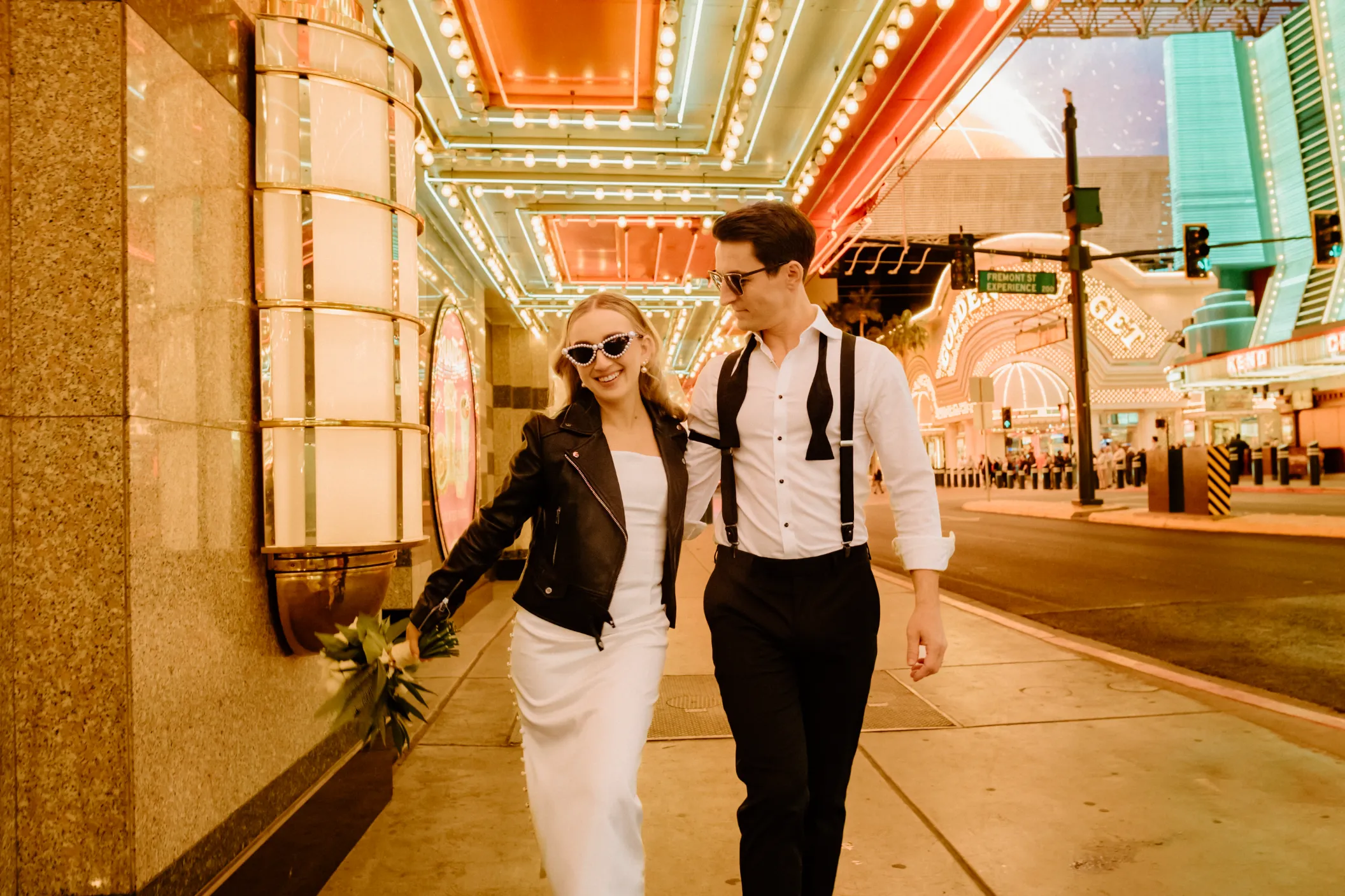 Paige and Lloyd's stylish Downtown Las Vegas elopement, couple strolling along illuminated Fremont Street Experience in edgy wedding attire