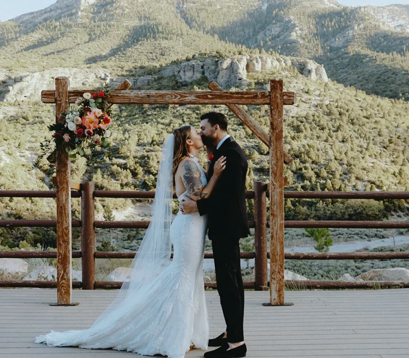 Abigail and Alex's rustic chic Mount Charleston wedding, couple sharing a tender moment under floral arch with panoramic mountain views near Las Vegas