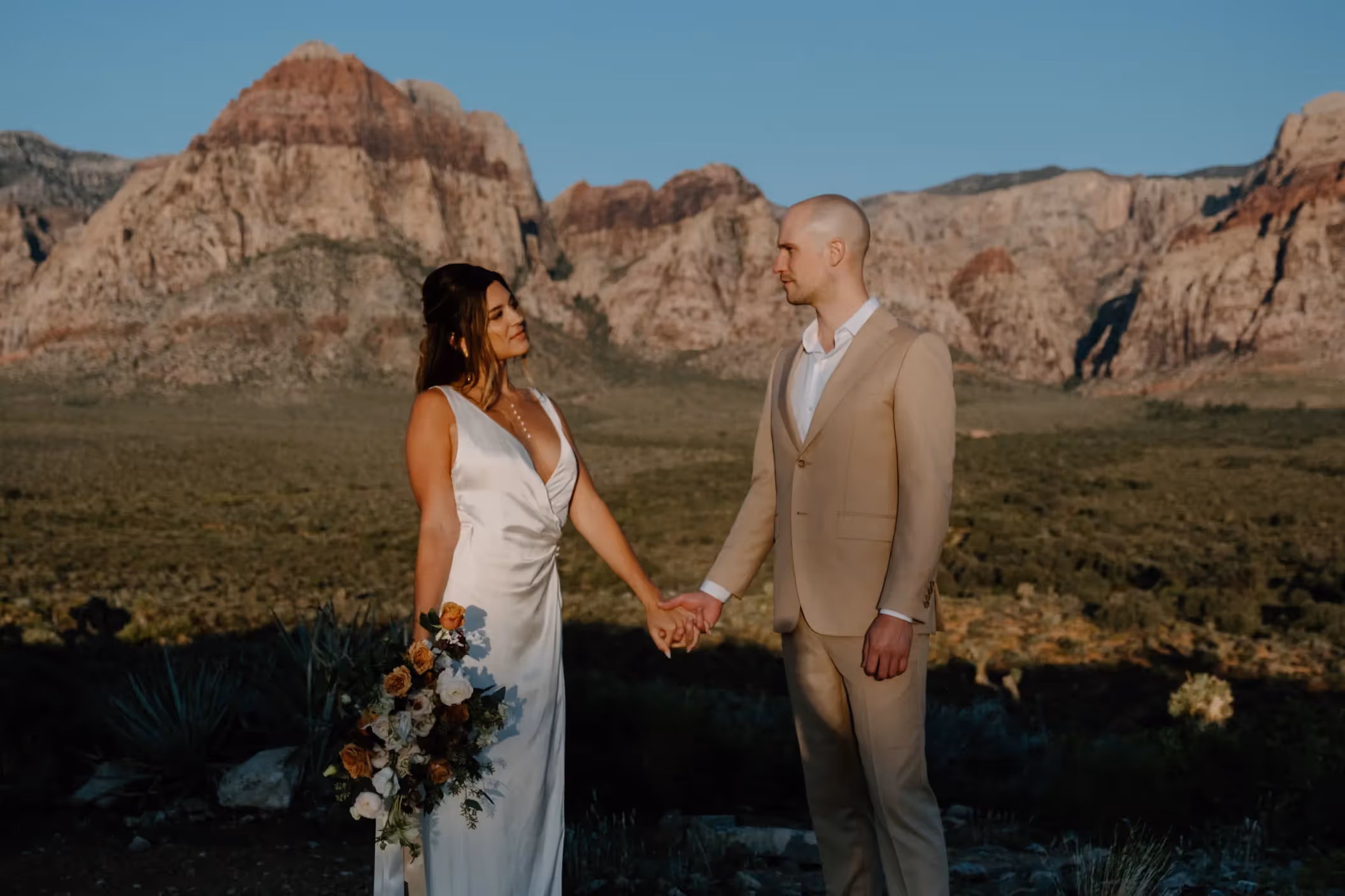 Brianna and Matthew hold each other close on red rock formations, showcasing scenic desert wedding backdrop near Las Vegas