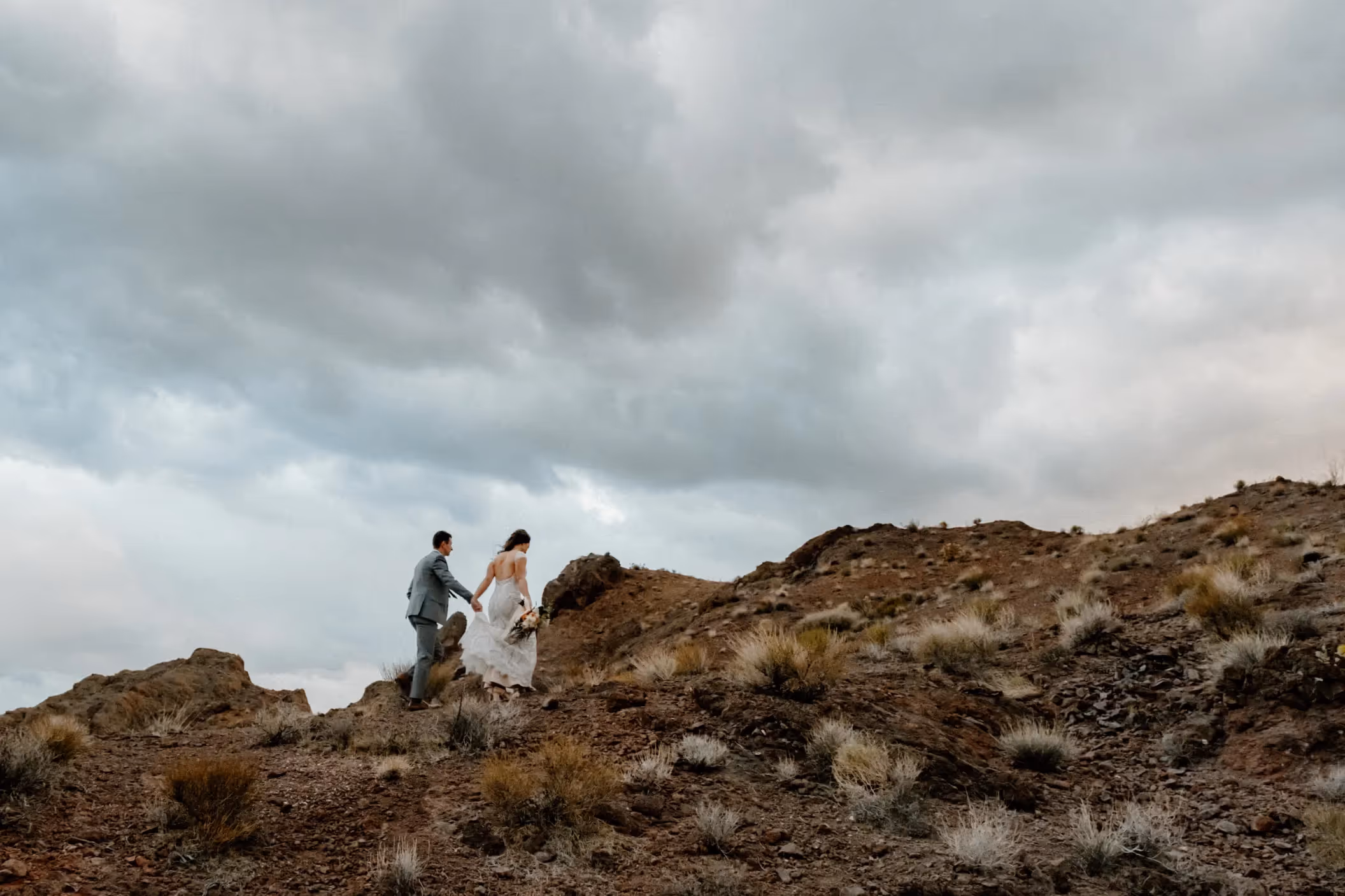 Adventurous desert elopement of Ashley and Joe near Las Vegas, couple hiking rocky terrain under dramatic stormy sky in Spring Mountains