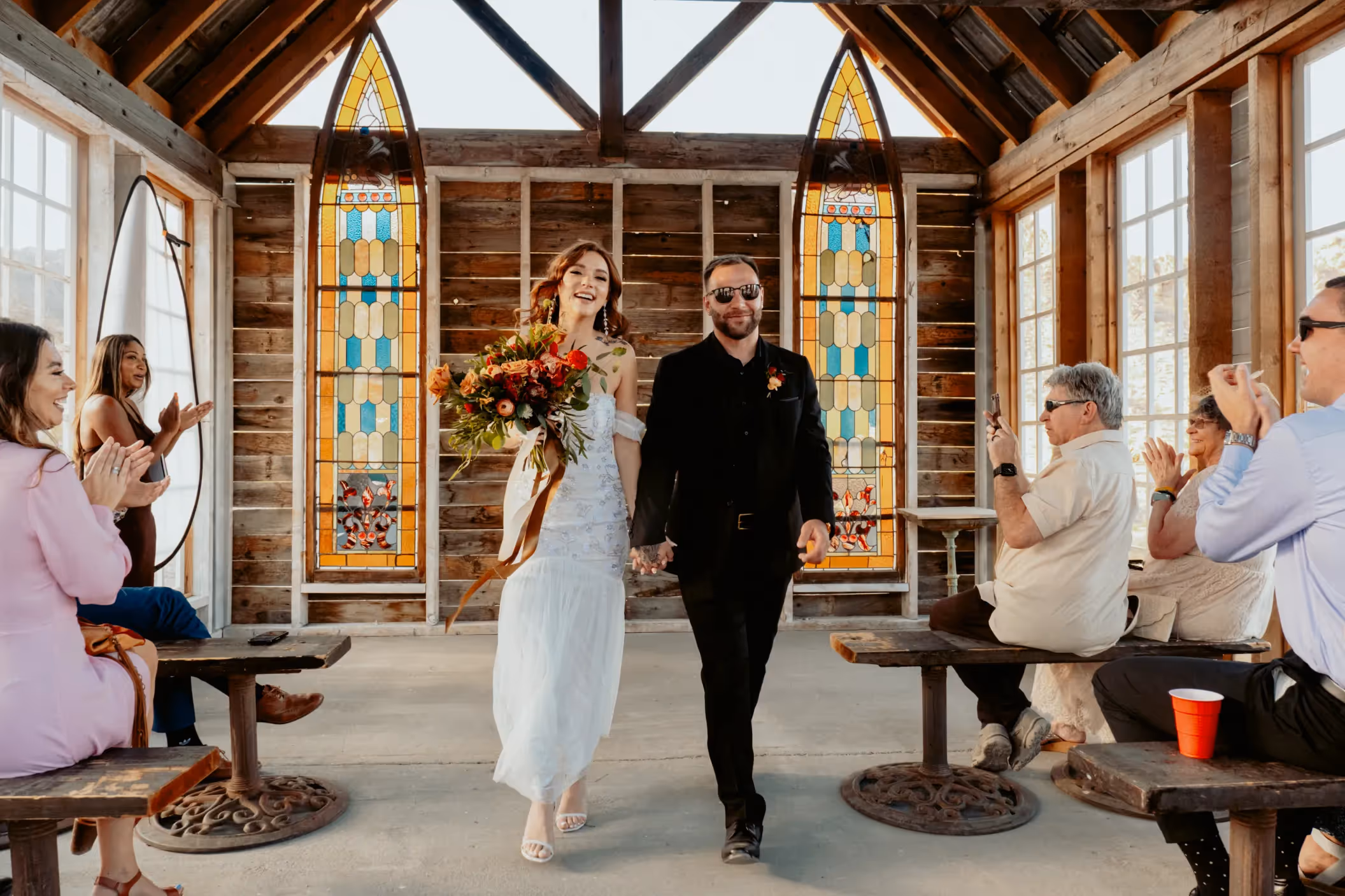 Rileigh and Jordan's intimate Las Vegas elopement in rustic chapel at Nelson Ghost Town, featuring colorful stained glass windows and joyful guests