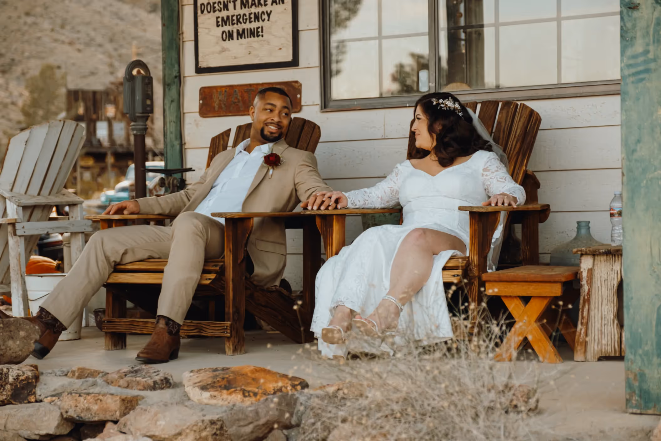 Relaxed Nelson Ghost Town elopement of Carrie and Lavar, newlyweds holding hands in Adirondack chairs on rustic porch near Las Vegas