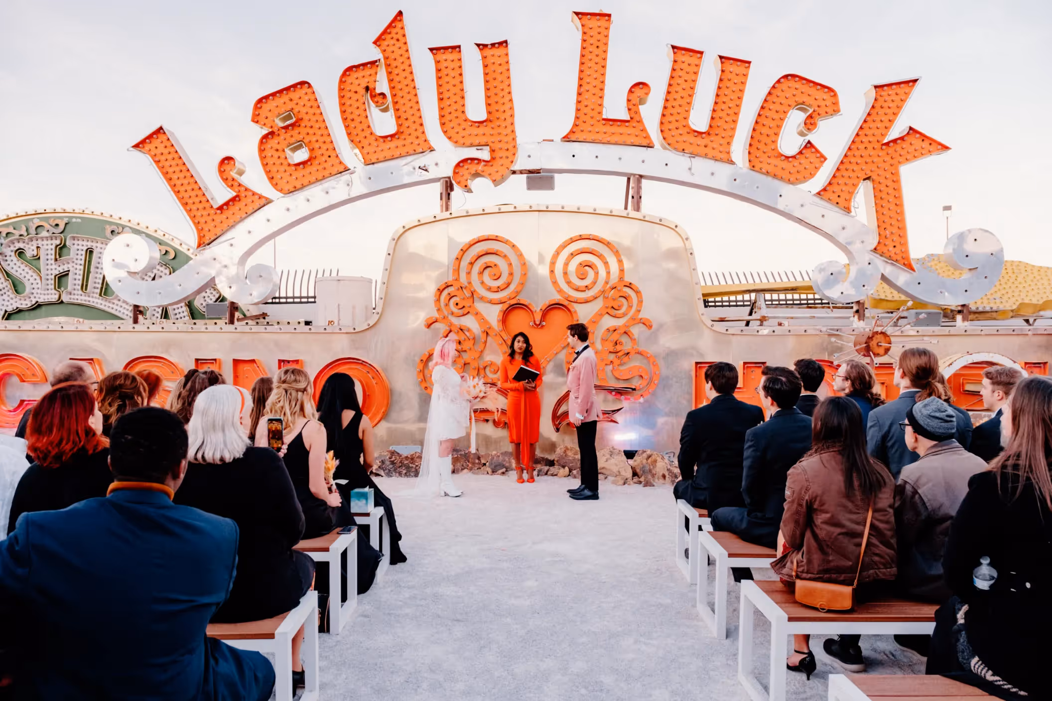 Sophia and Ryan's vibrant Las Vegas elopement ceremony at the Neon Museum, exchanging vows under iconic 'Lady Luck' sign with guests seated