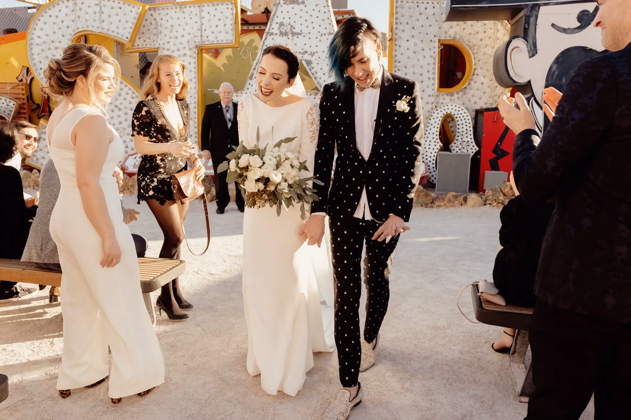Amanda and Josh's stylish Las Vegas elopement at the Neon Museum, joyfully exiting their ceremony surrounded by vintage neon signs and smiling guests