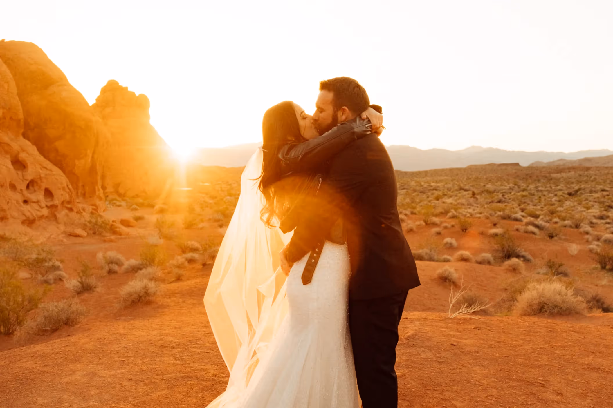 Nat and Ace's romantic sunset elopement at Valley of Fire, sharing a passionate kiss against a backdrop of red rock formations and golden desert light