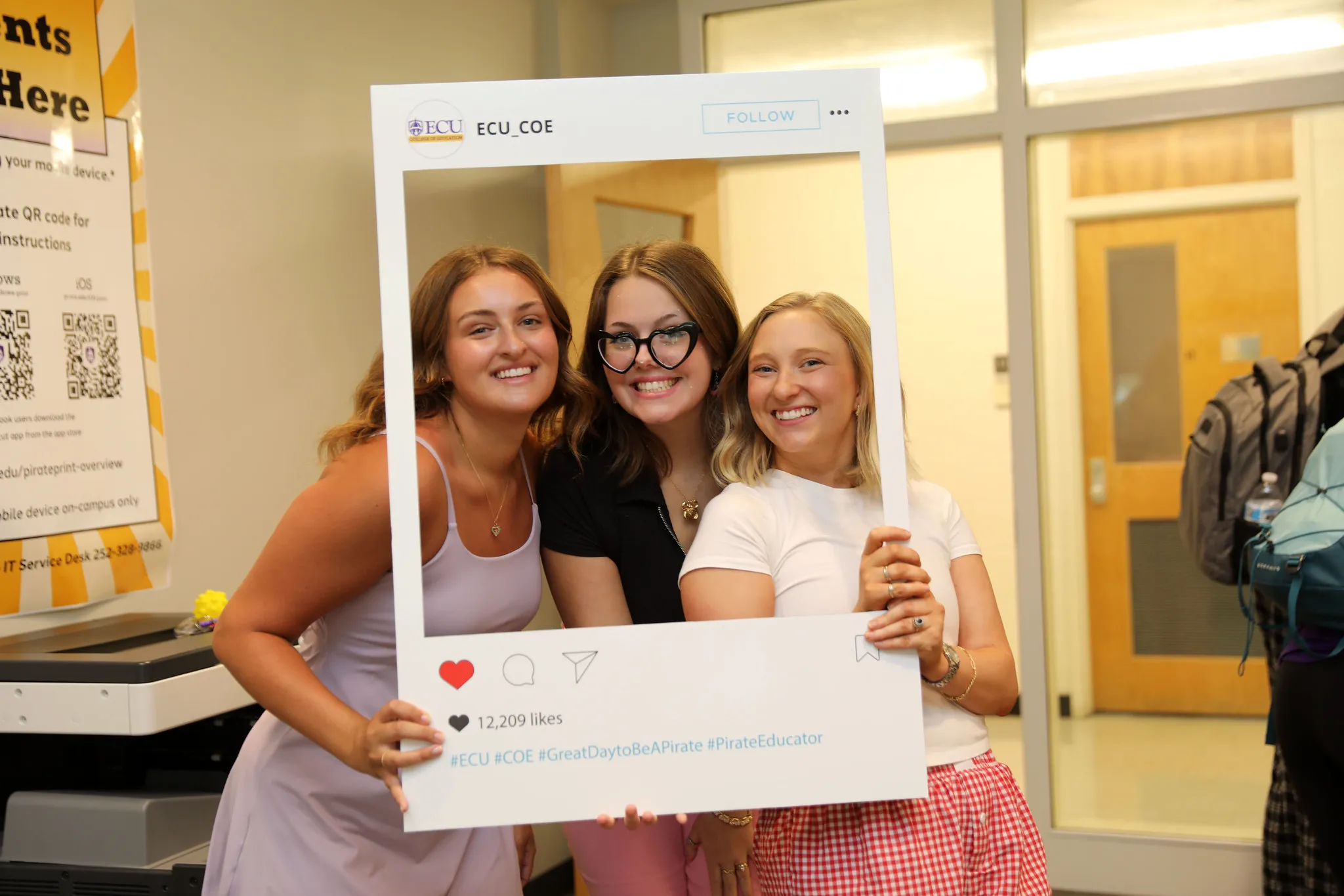 Three students posing together in an ECU social media photo frame