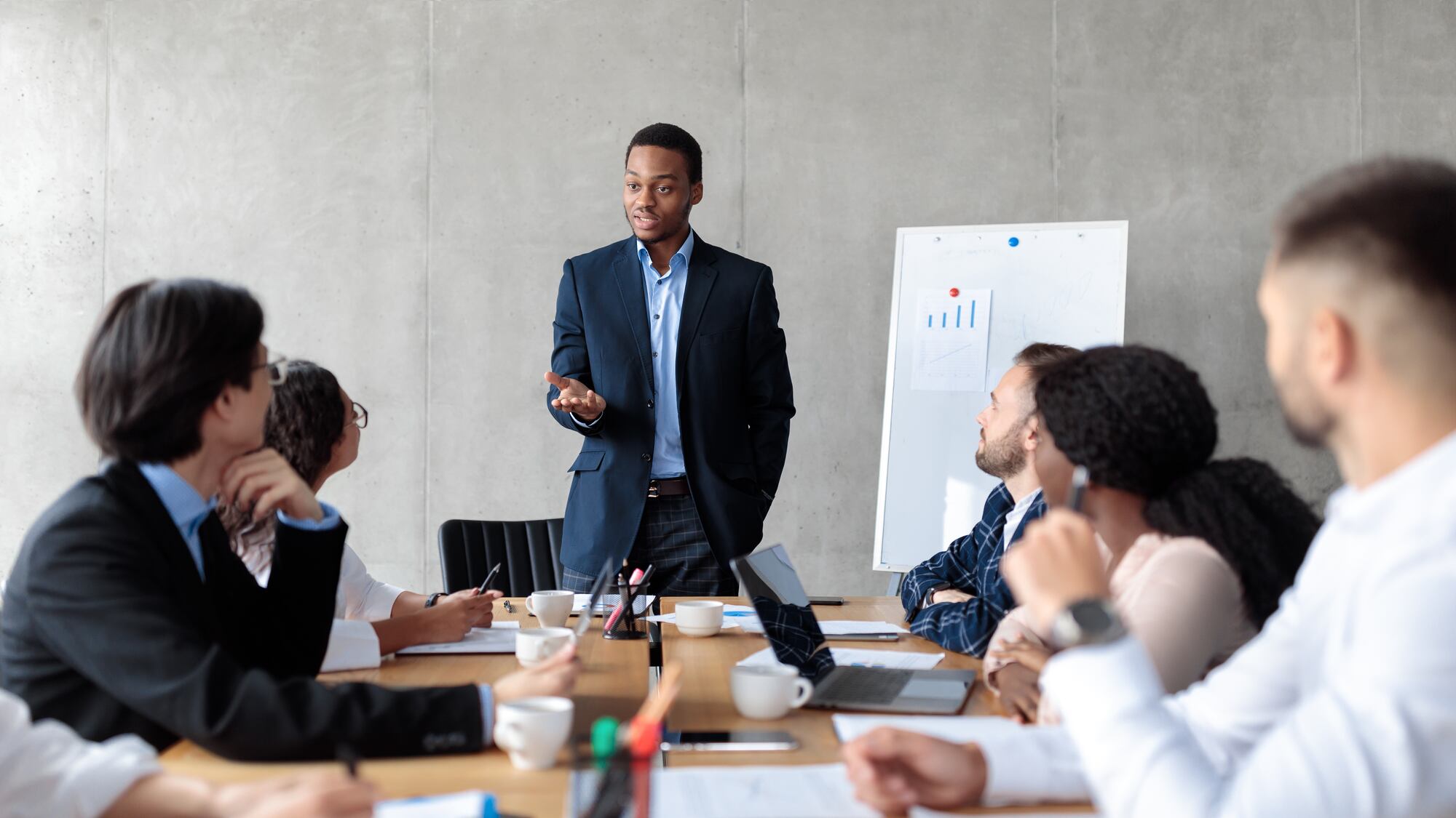man standing giving a presentation to colleagues seated at a conference room table