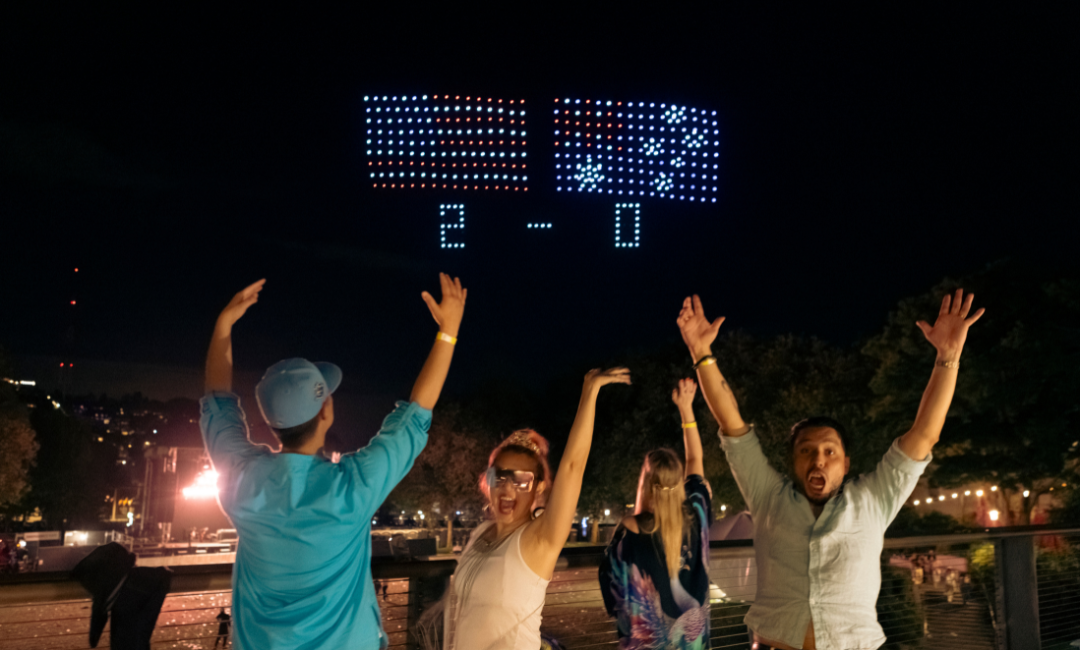 people celebrating in front of the drone show scoreboard with US and Australia flags