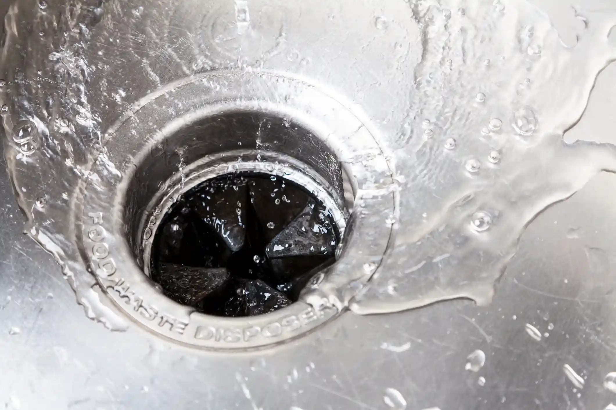 Close-up of kitchen sink drain with water flowing into food waste disposer