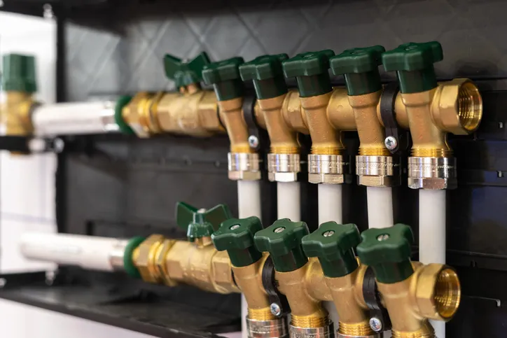 Brass water valves with green handles mounted on black panel in plumbing setup