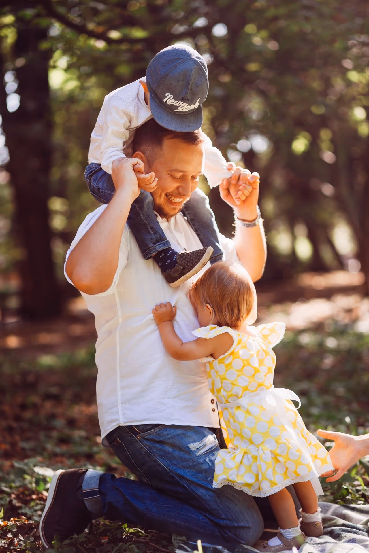 Father playing with his two young children in a sunny park.