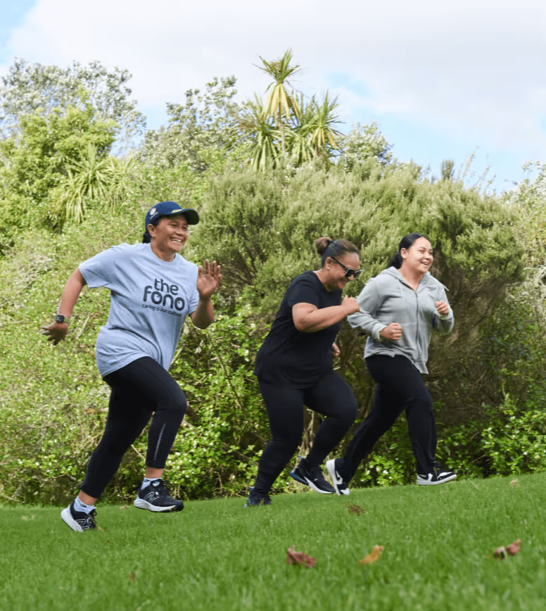 Three individuals are jogging on a grassy path, surrounded by lush greenery and trees under a partly cloudy sky.