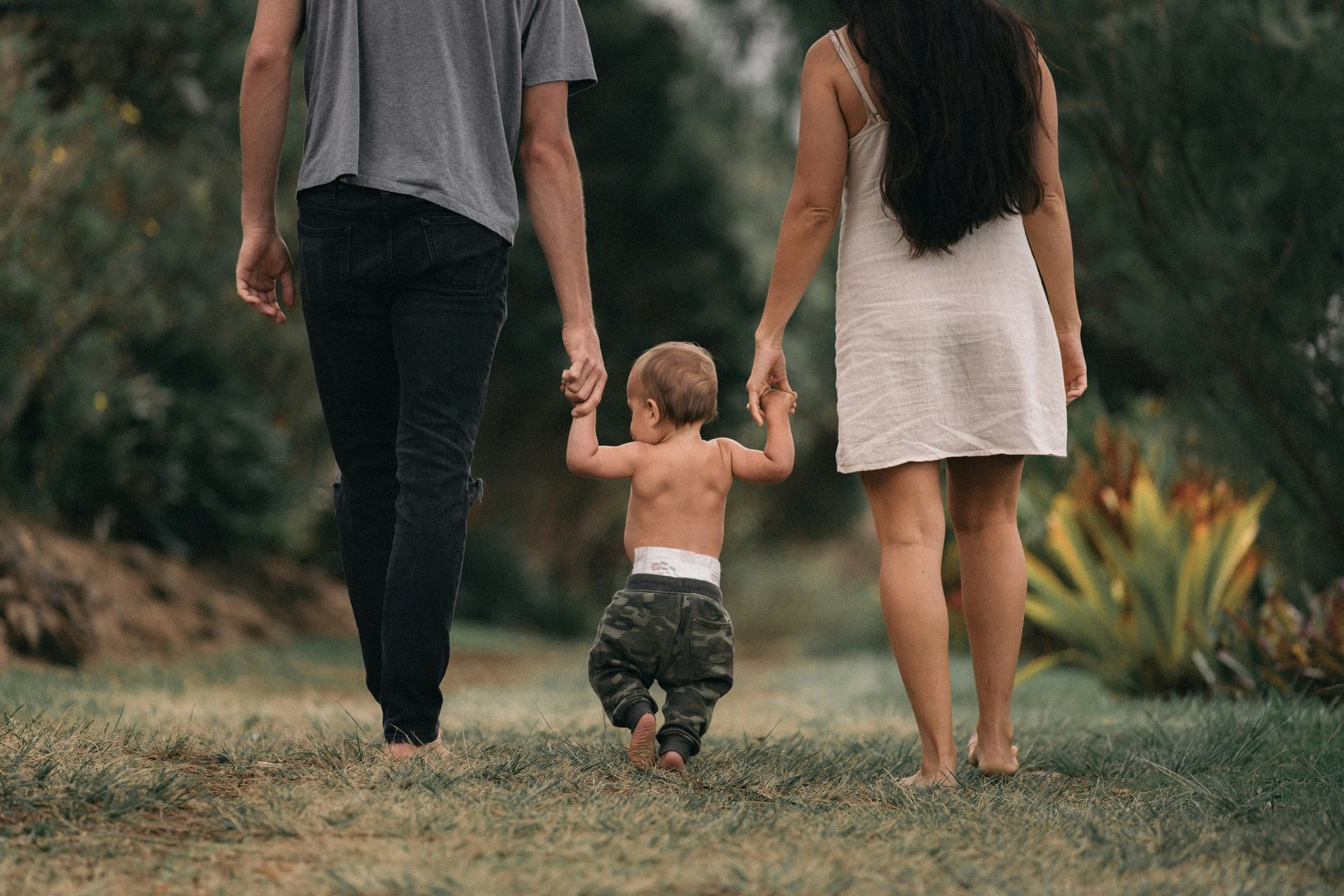 A smiling man holds two children, a girl on his left shoulder and a boy on his right, in front of a white picket fence.